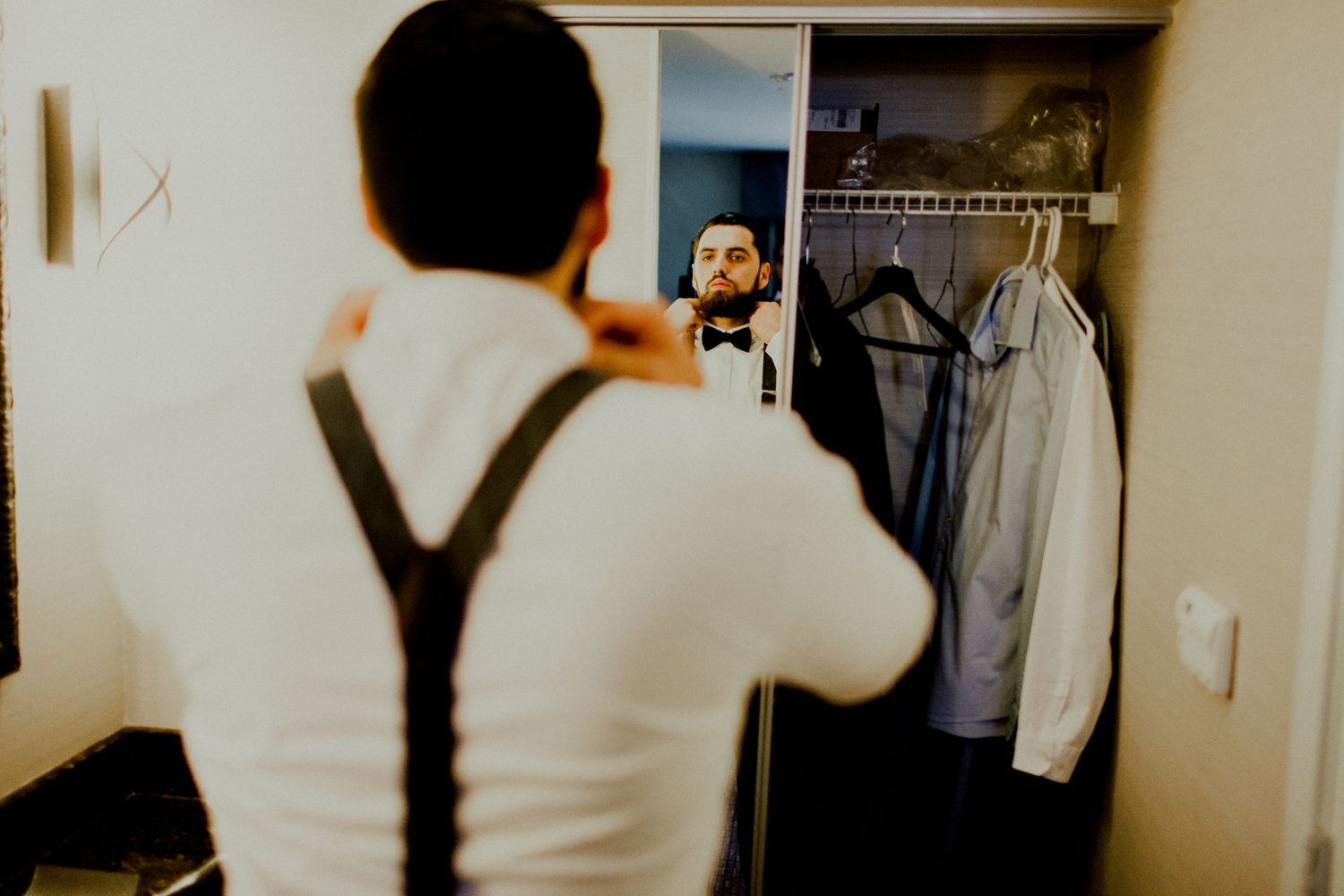 groom adjusting bow tie in front of mirror