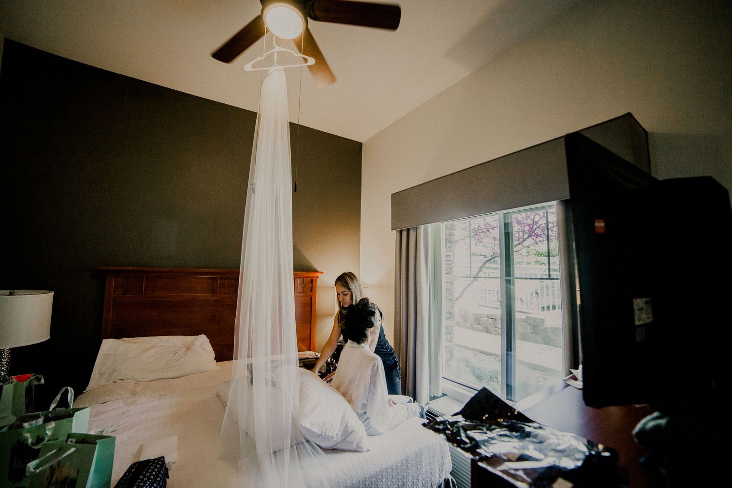 bride getting ready with makeup artist at holiday inn with veil hanging from ceiling