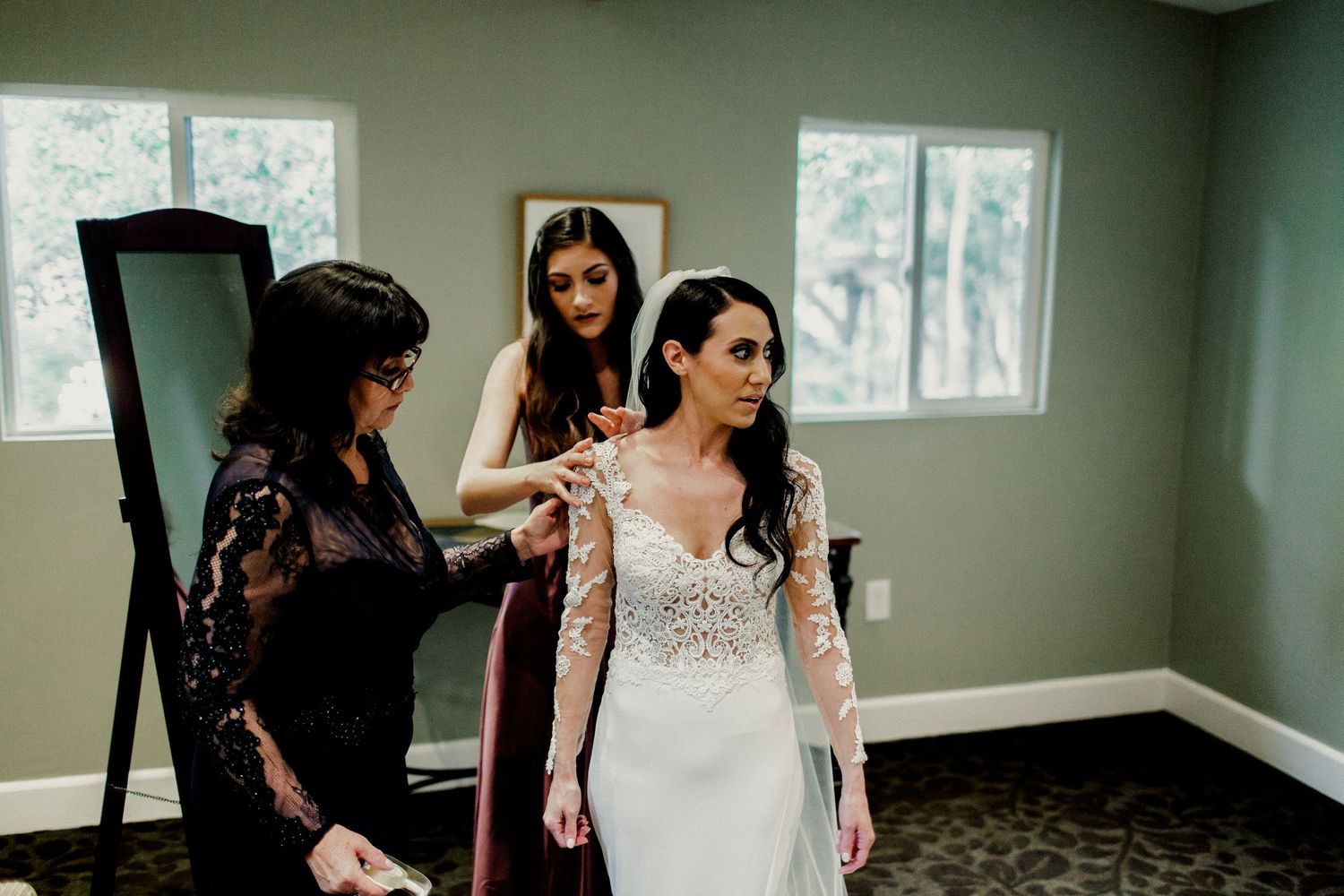 mom and sister helping bride put on wedding dress