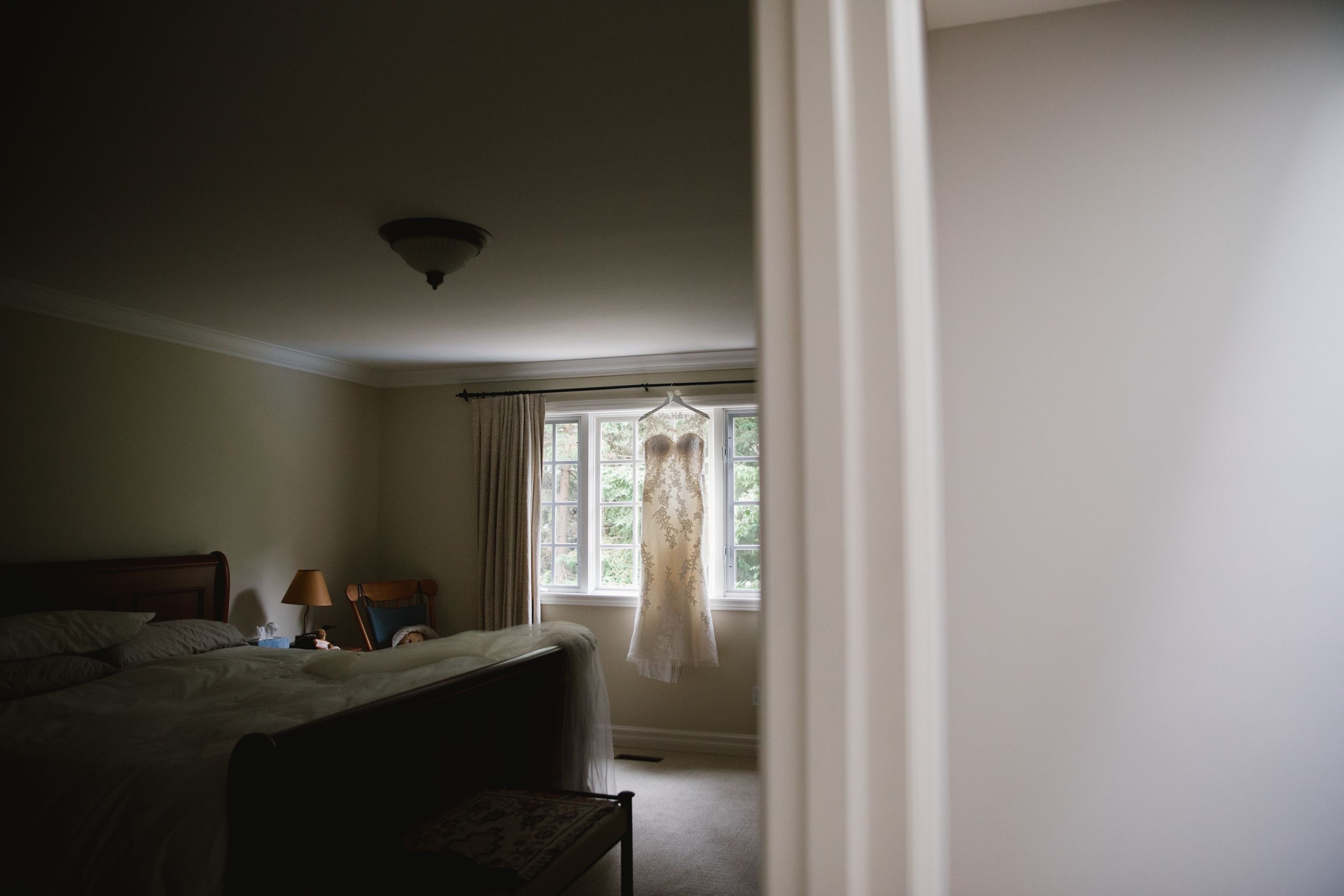 wedding dress hung in window of a dark bedroom