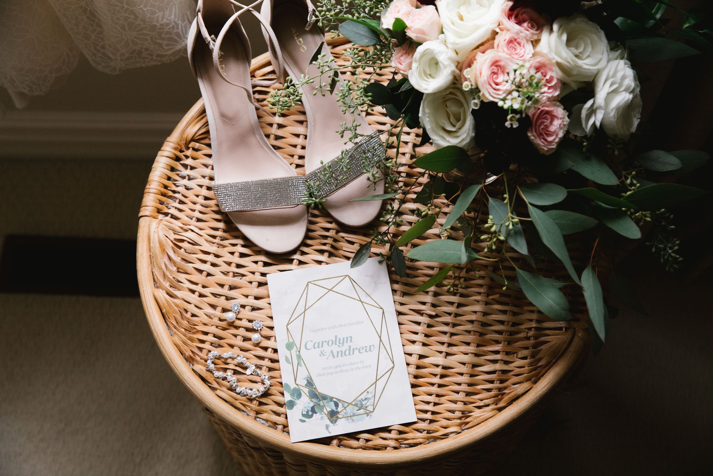 wedding details, bridal shoes, invitation, jewelry and bouquet on a wicker hamper