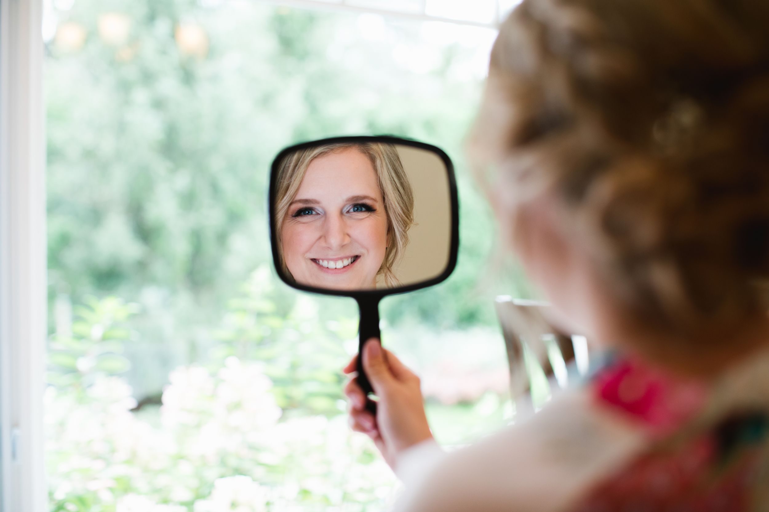 bride looking into hand mirror and smiling
