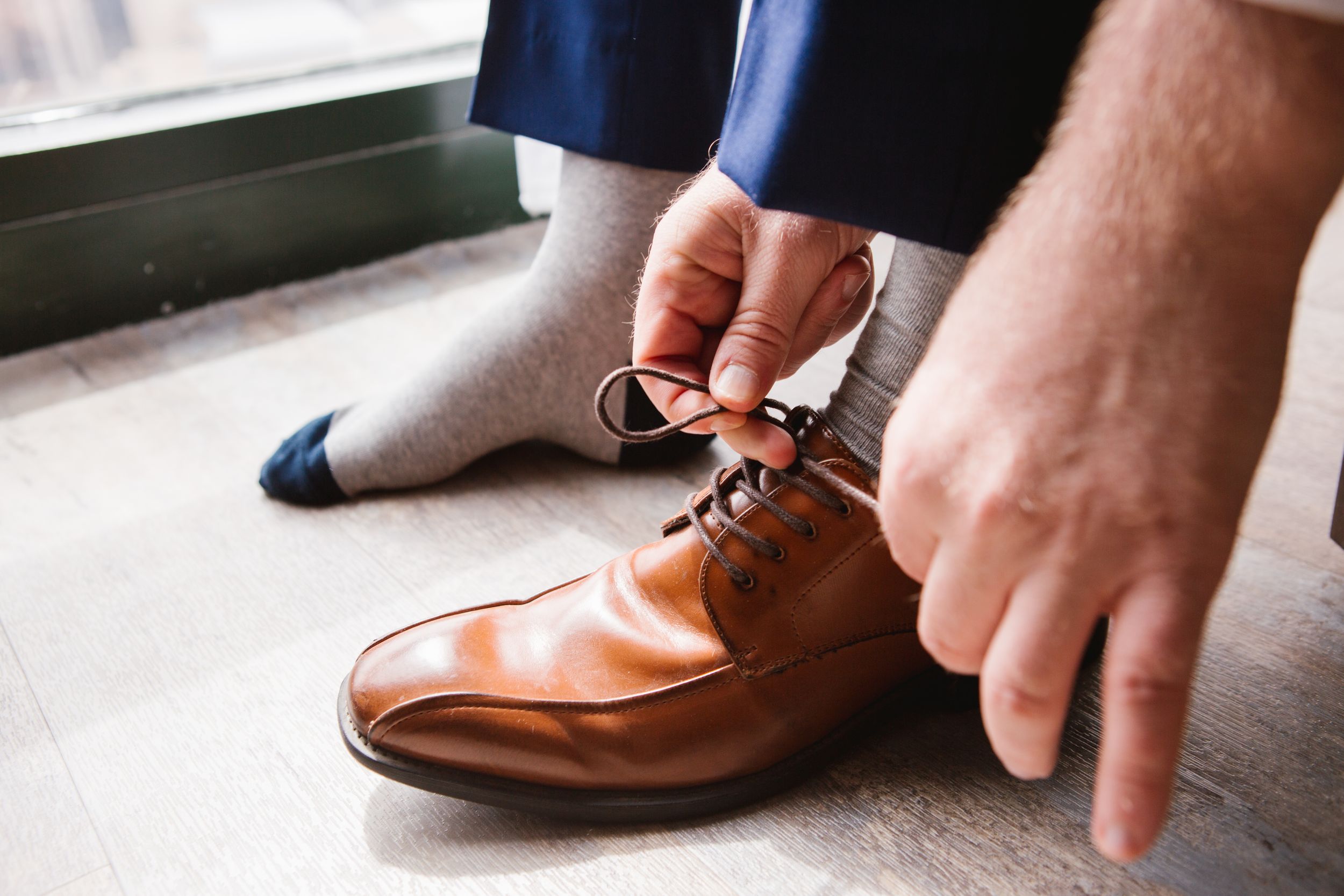 close up of groom tying shoelace on his brown wedding shoes