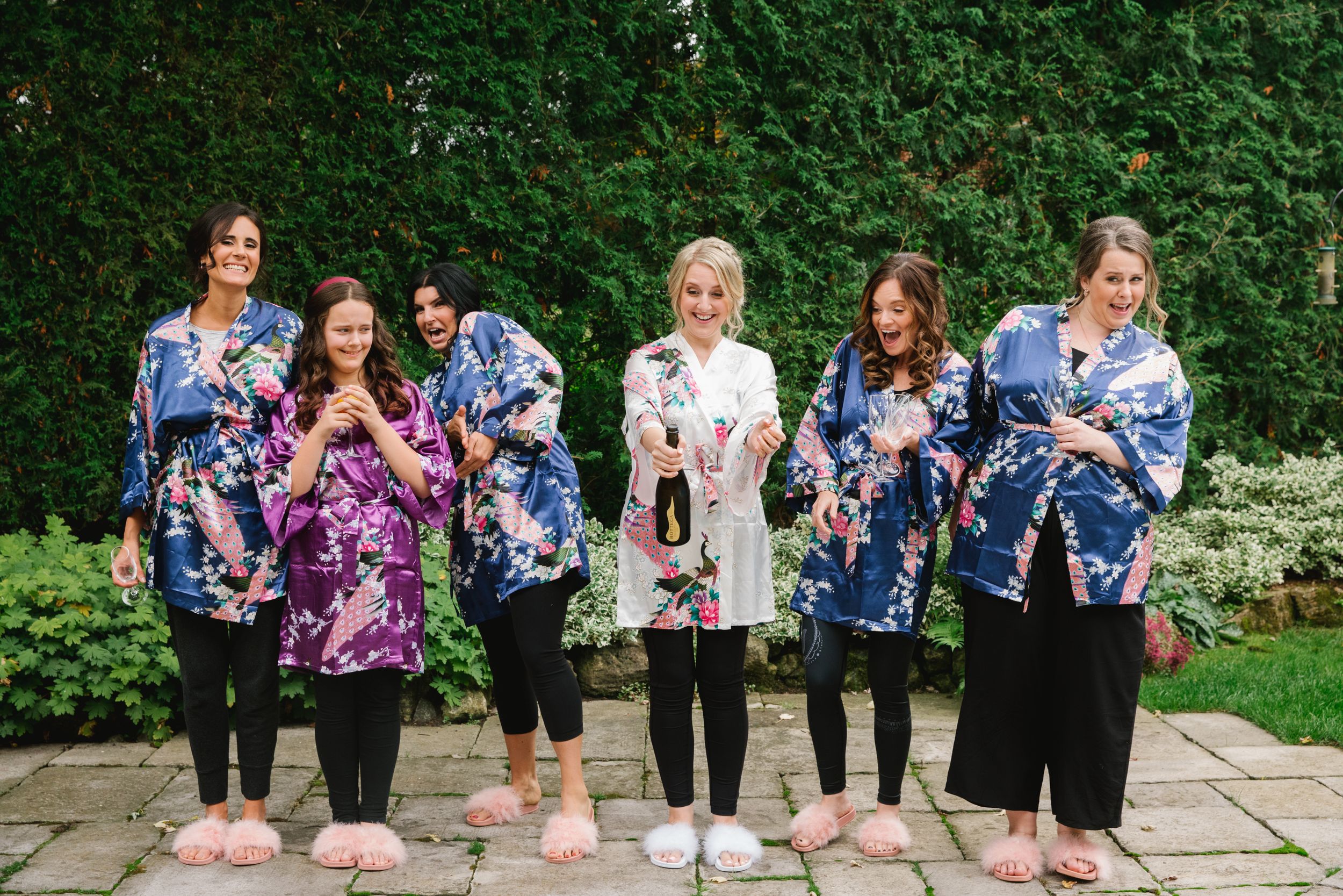 bride and bridesmaids in colourful robes popping champagne in backyard
