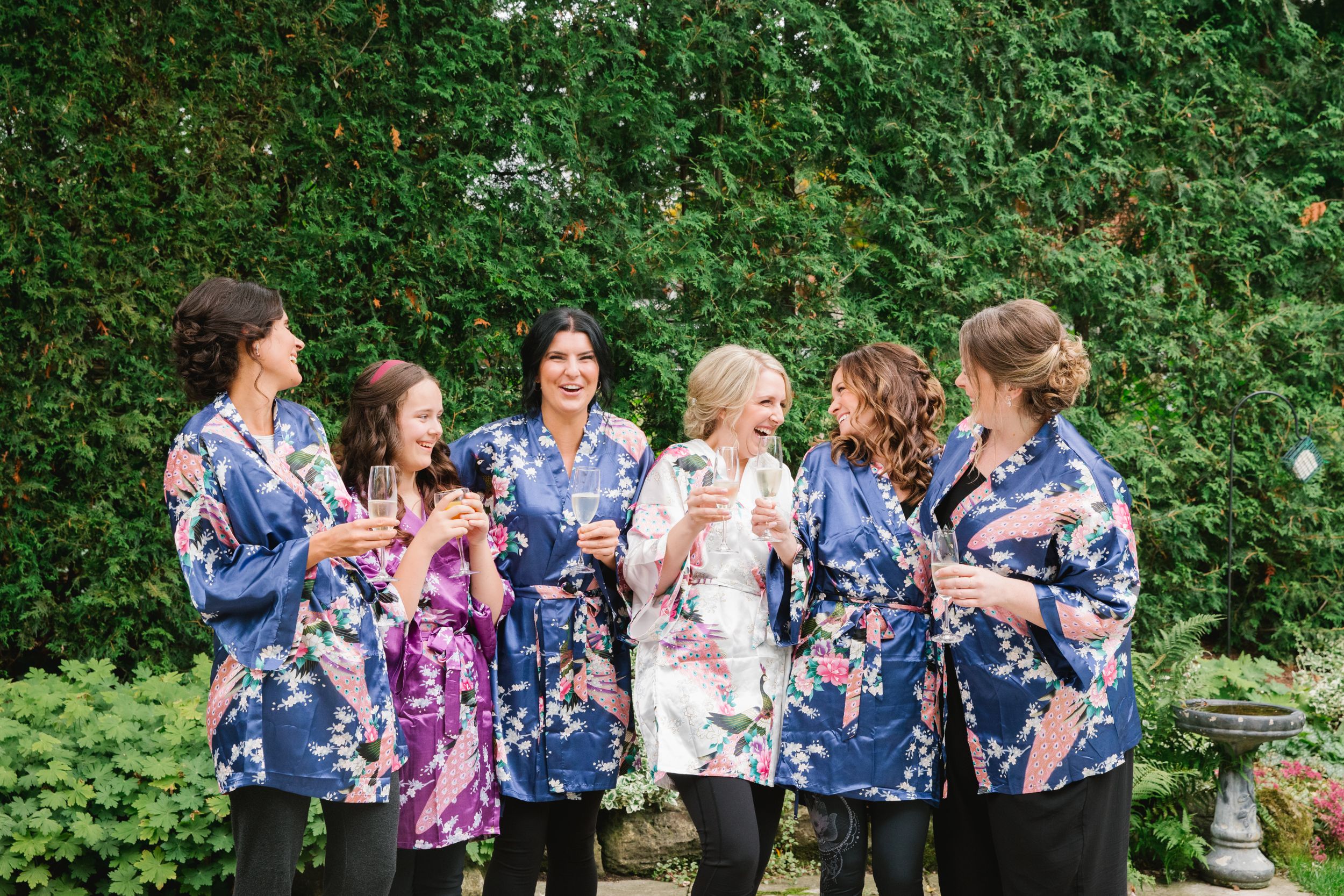 bride and bridesmaids in colourful robes holding champagne and laughing in backyard