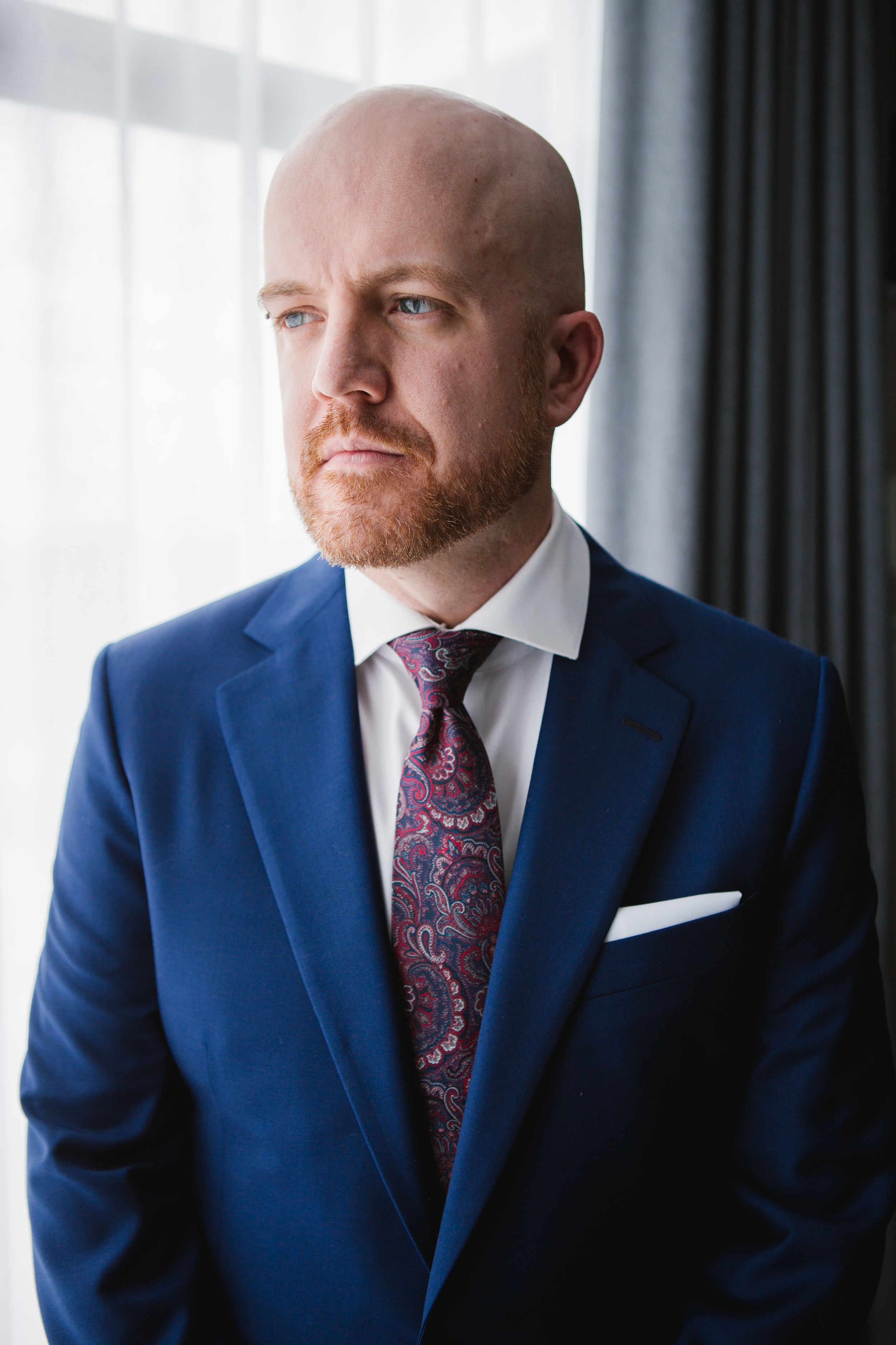 groom wearing blue suit and purple tie looking out window