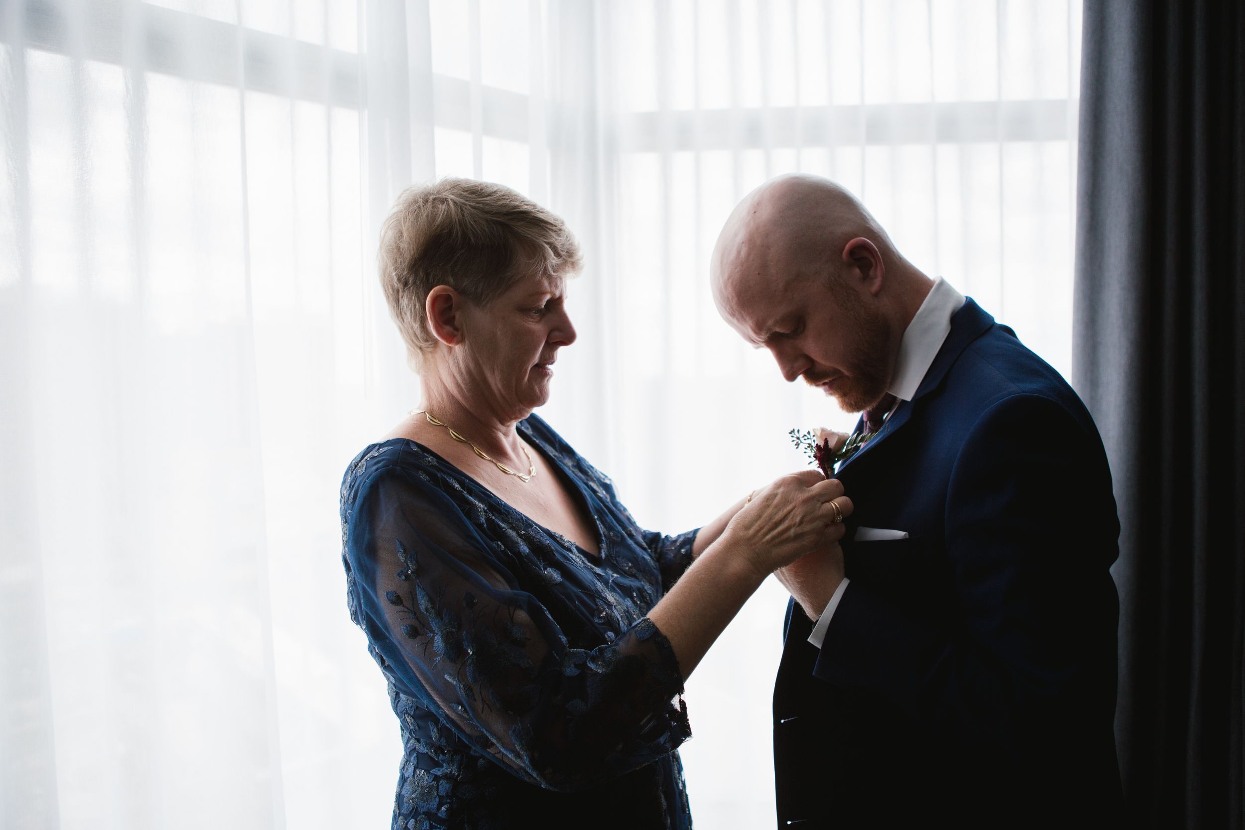 mother of groom in blue dress helping with boutonniere