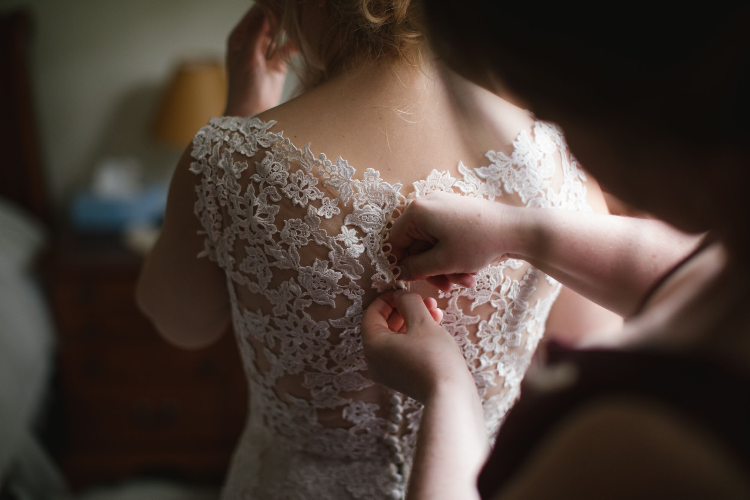 close up of bridesmaid buttoning up wedding dress in thornhill