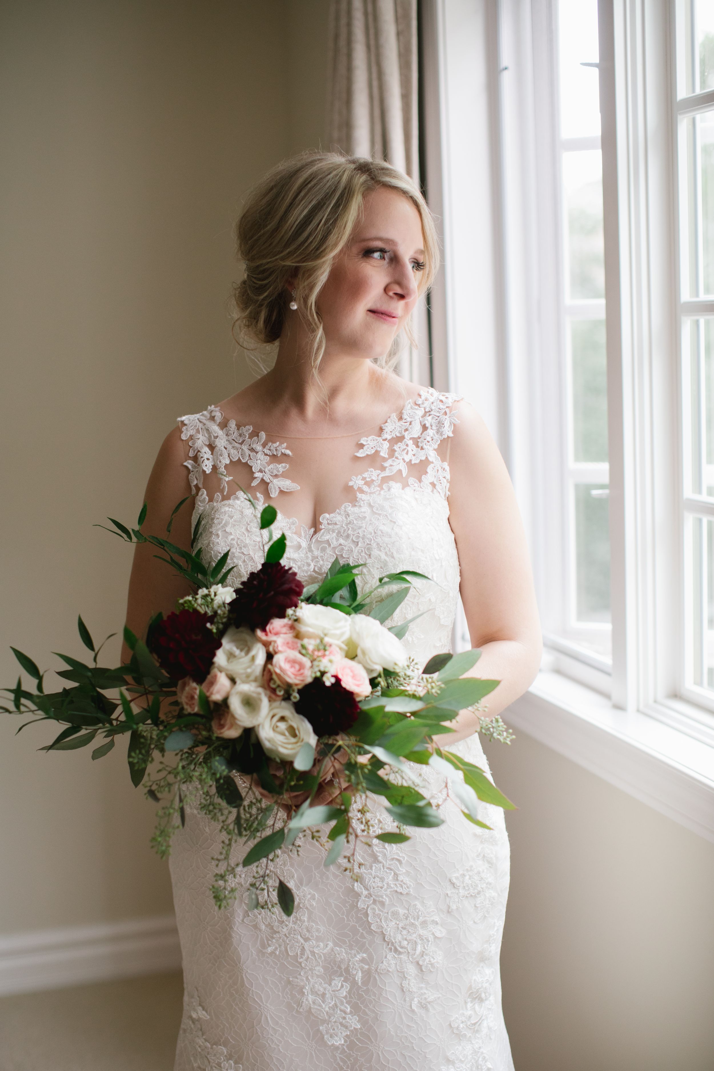bride holding her burgundy and pink bouquet and looking out of the window