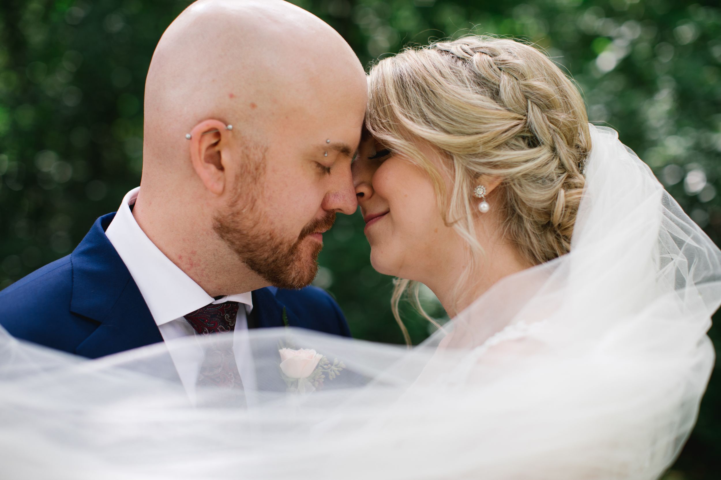 bride and groom close up kissing with veil flowing in the wind in park
