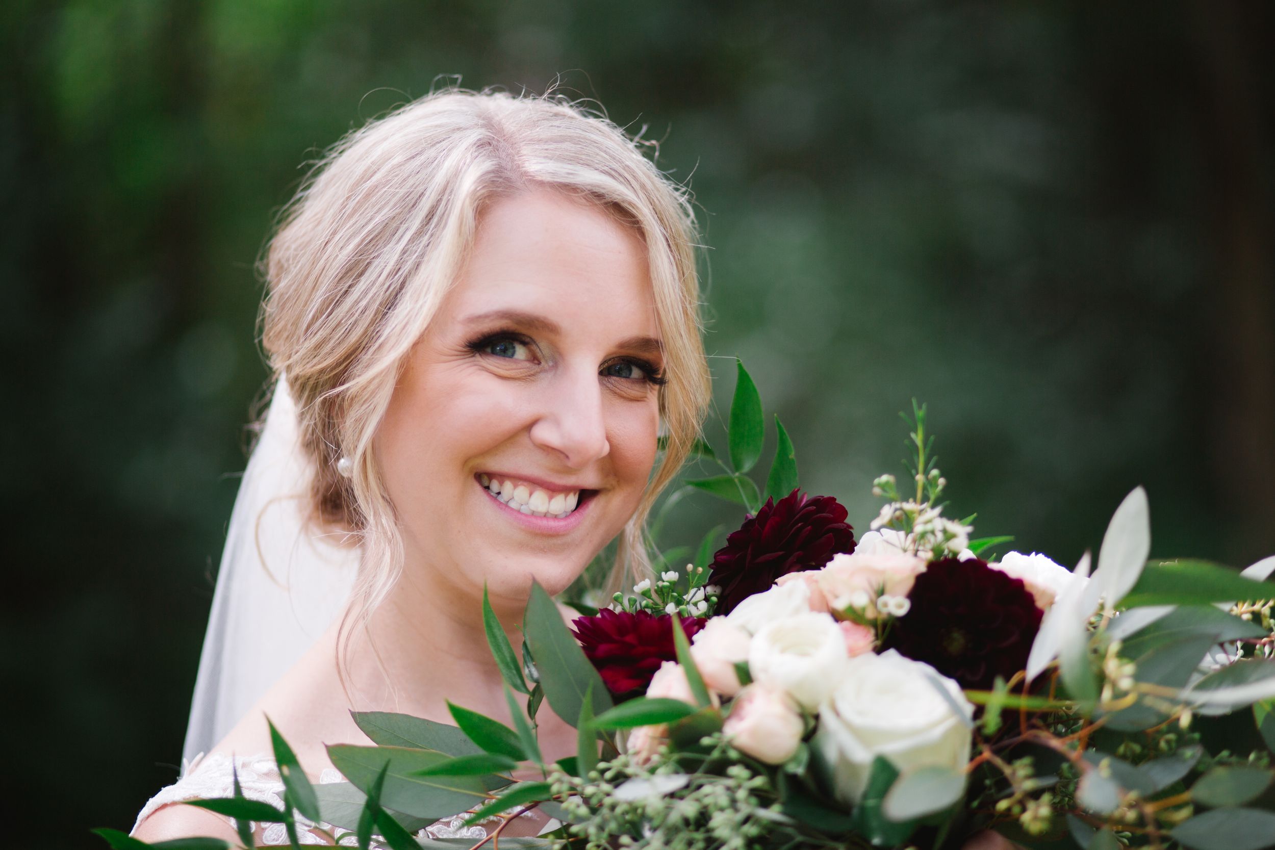 blonde bride smiling at her bouquet of burgundy and pink flowers