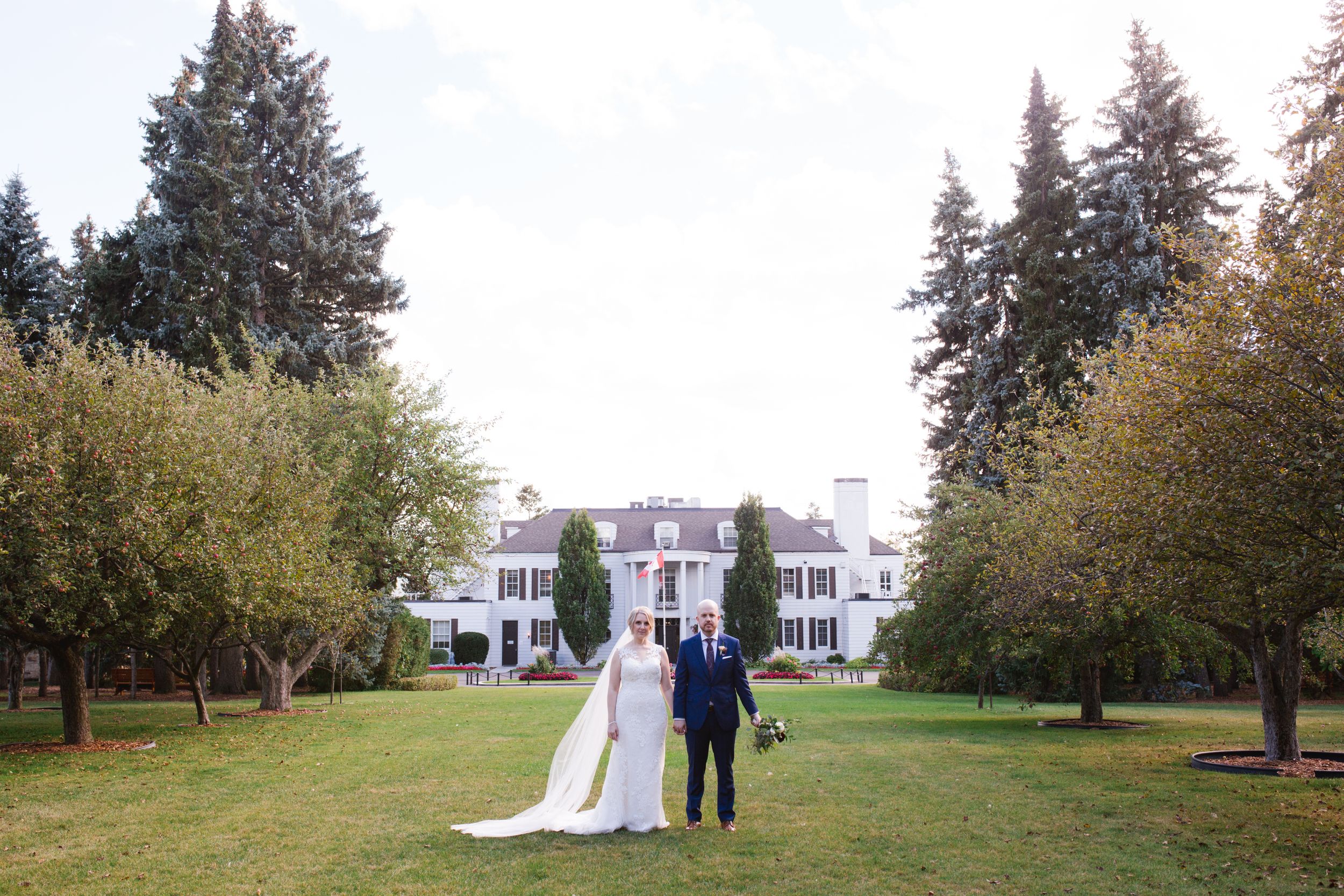 bride and groom in front of white building with columns and trees on either side shouldice hospital thornhill
