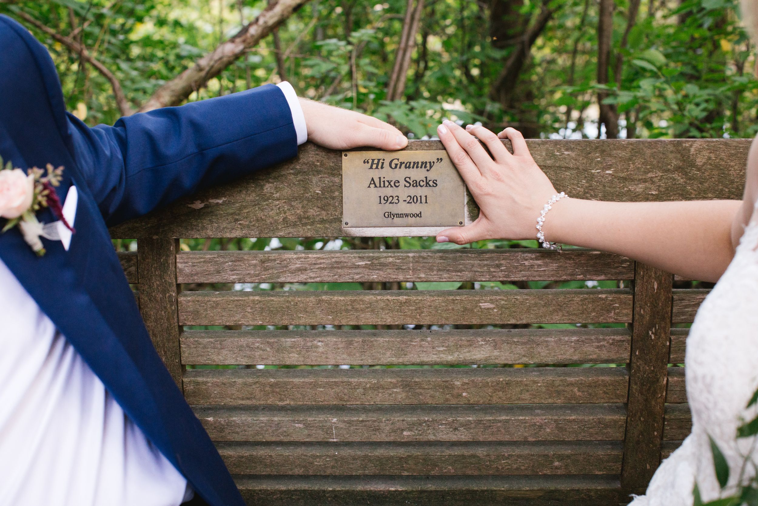 bride and groom holding plaque of relative that passed away on park bench