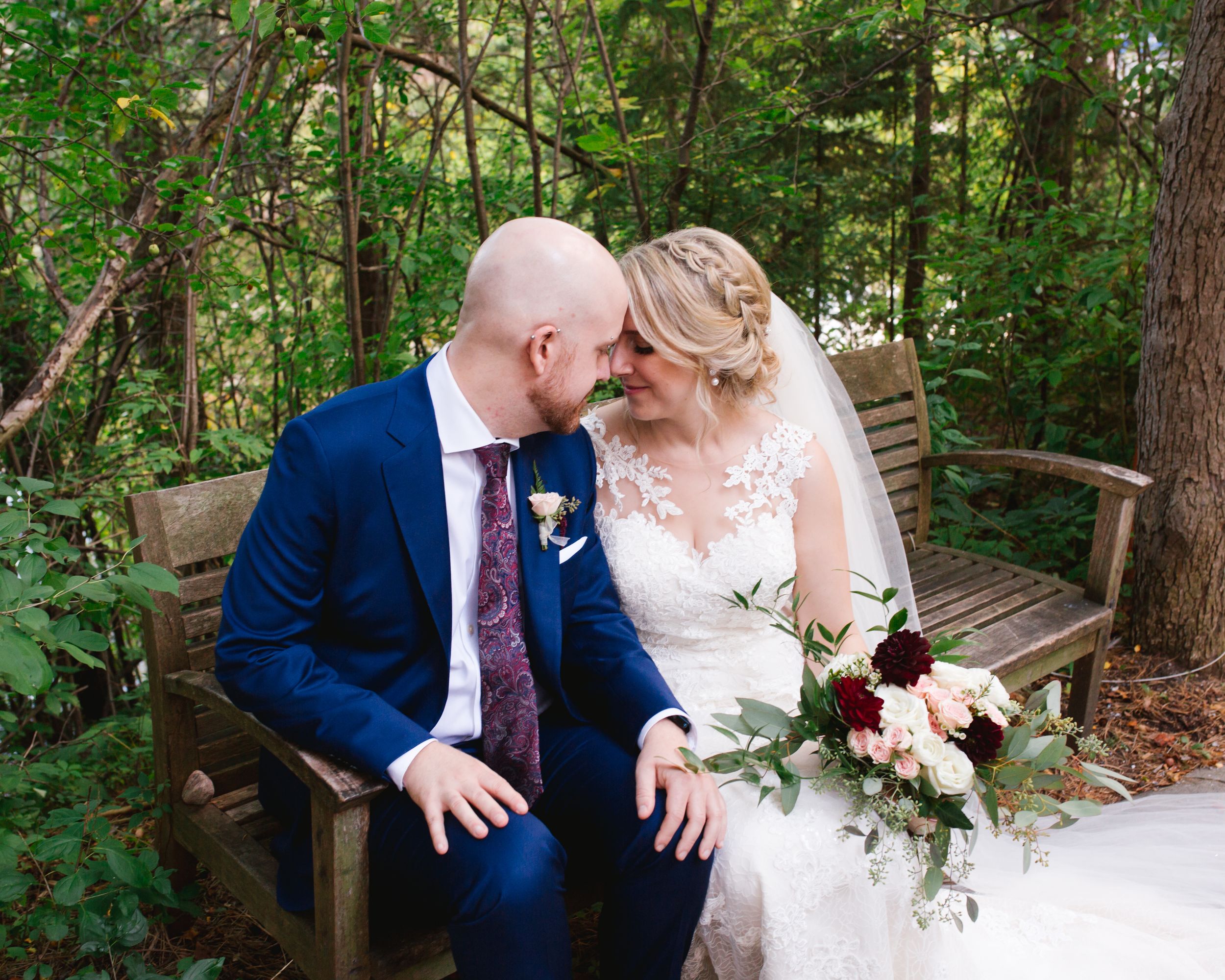bride and groom sitting on bench in park and snuggling