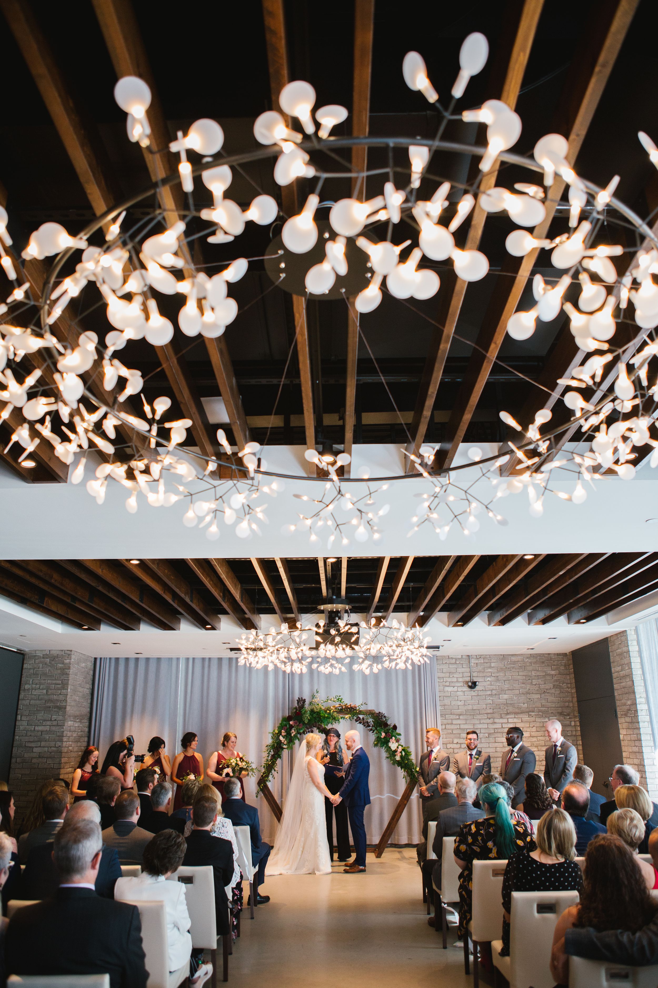 bride and groom holding hands at the altar with light installation above indoor ceremony