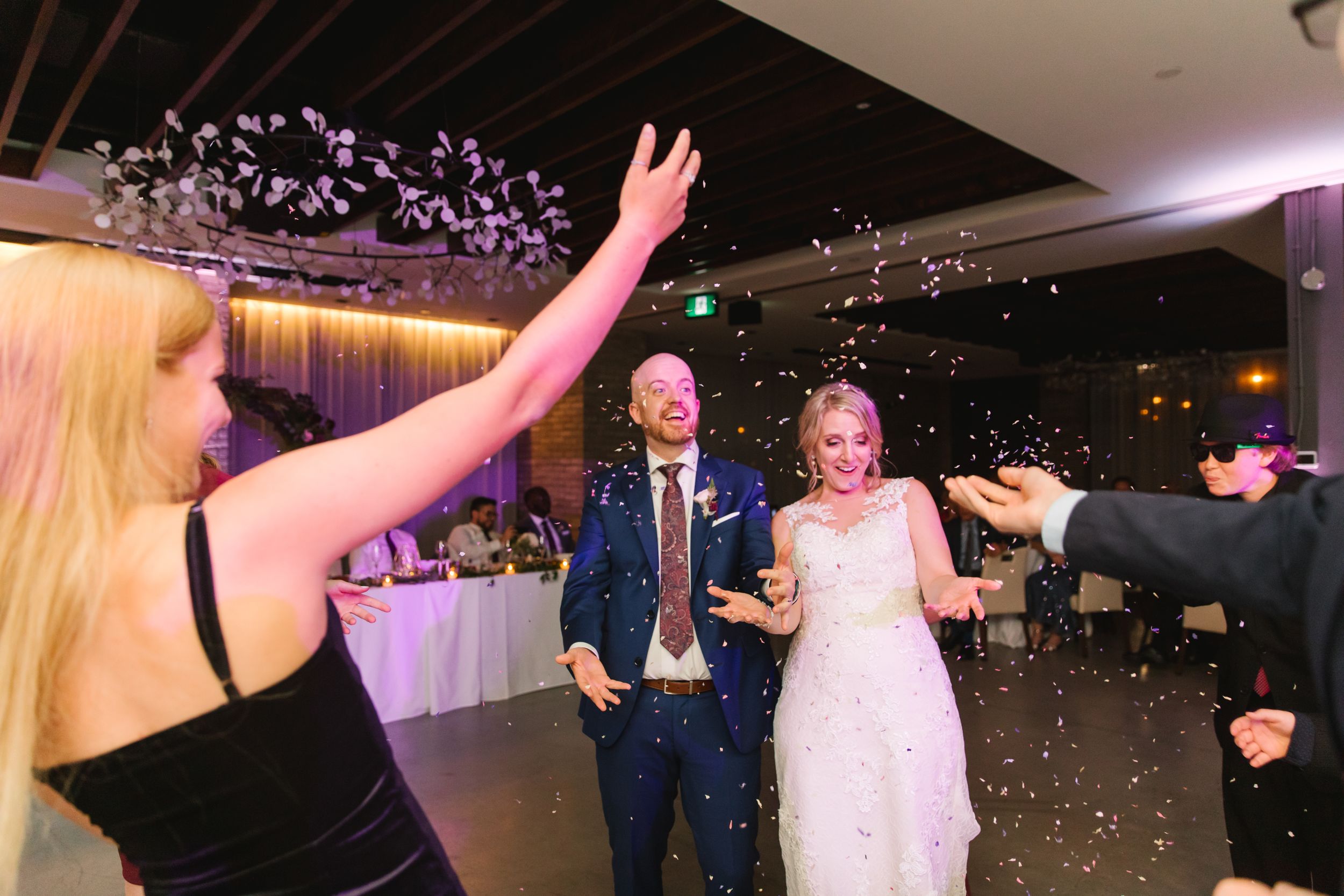 guests throw confetti on bride and groom who are surprised at reception