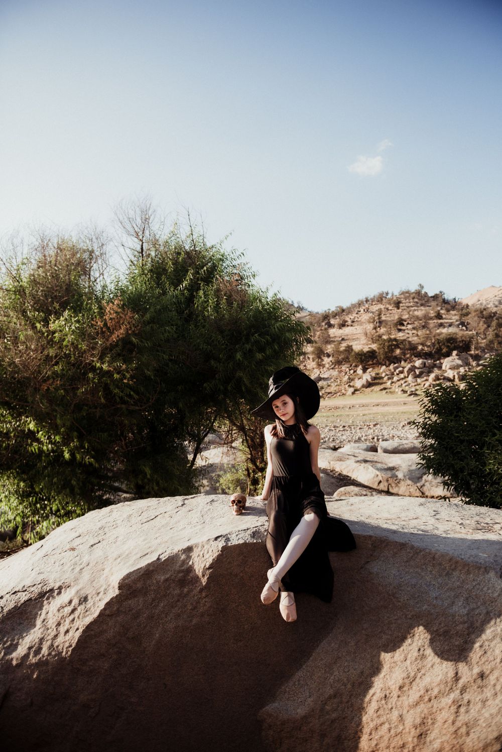 Girl dressed like a witch and posing on a boulder next to a skull for a Halloween photoshoot in Three Rivers California