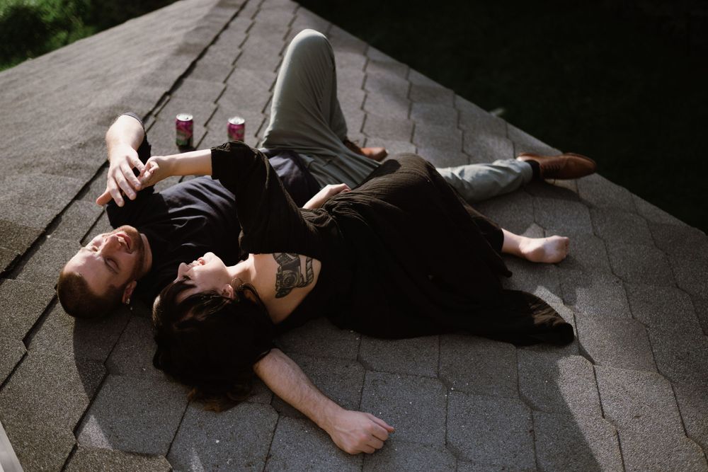 couple-laying-on-house-roof-drinking-beer-laughing-winterset-iowa-raelyn-ramey-photography