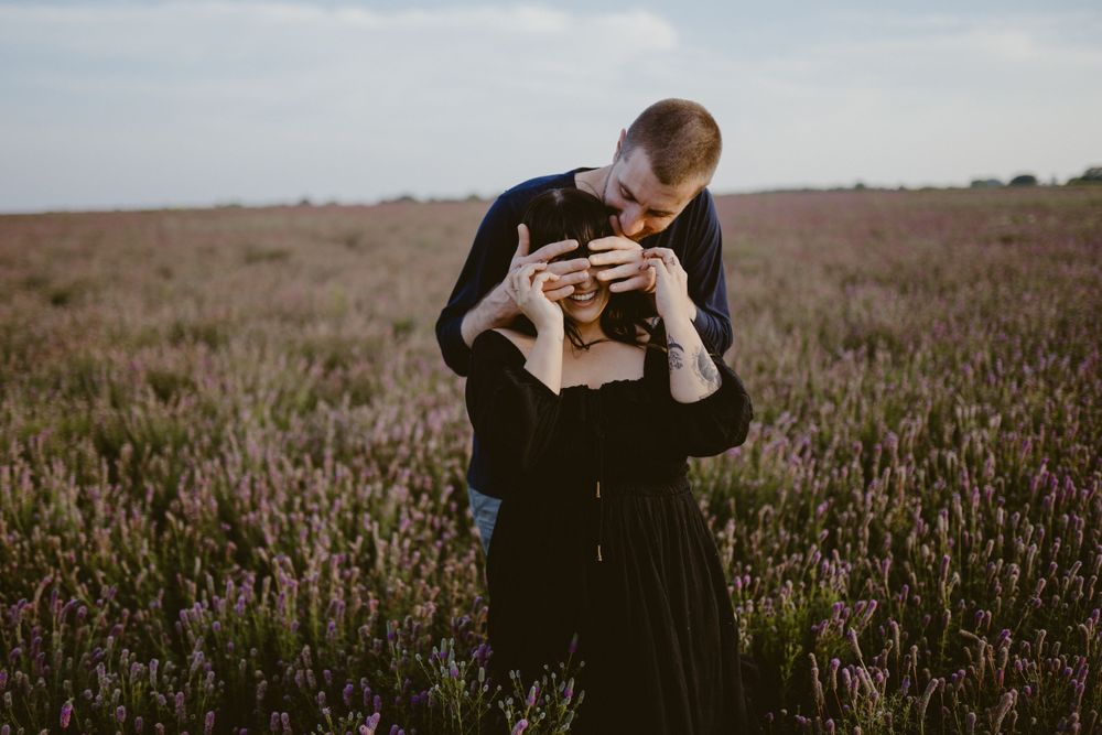 fiance-covering-womans-eyes-in-flower-field-laughing-winterset-iowa-raelyn-ramey-photography