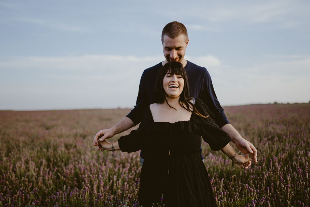 couple-holding-hands-playing-airplane-in-flower-field-winterset-iowa-raelyn-ramey-photography