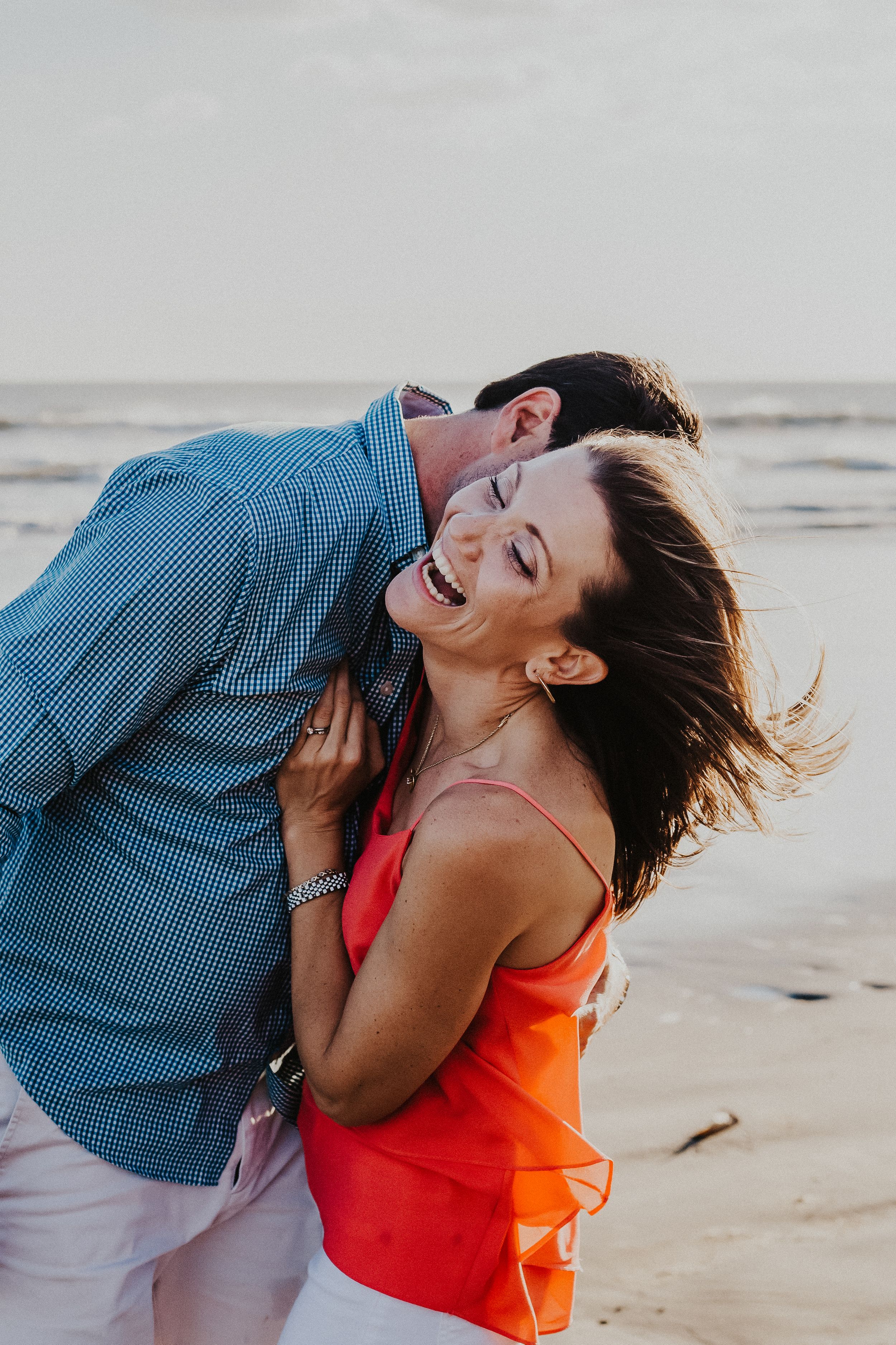 husband and wife embrace on the beach while laughing