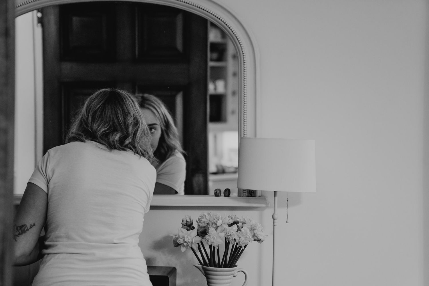 Black and white photo of a bridesmaid doing her make up in a large mirror.