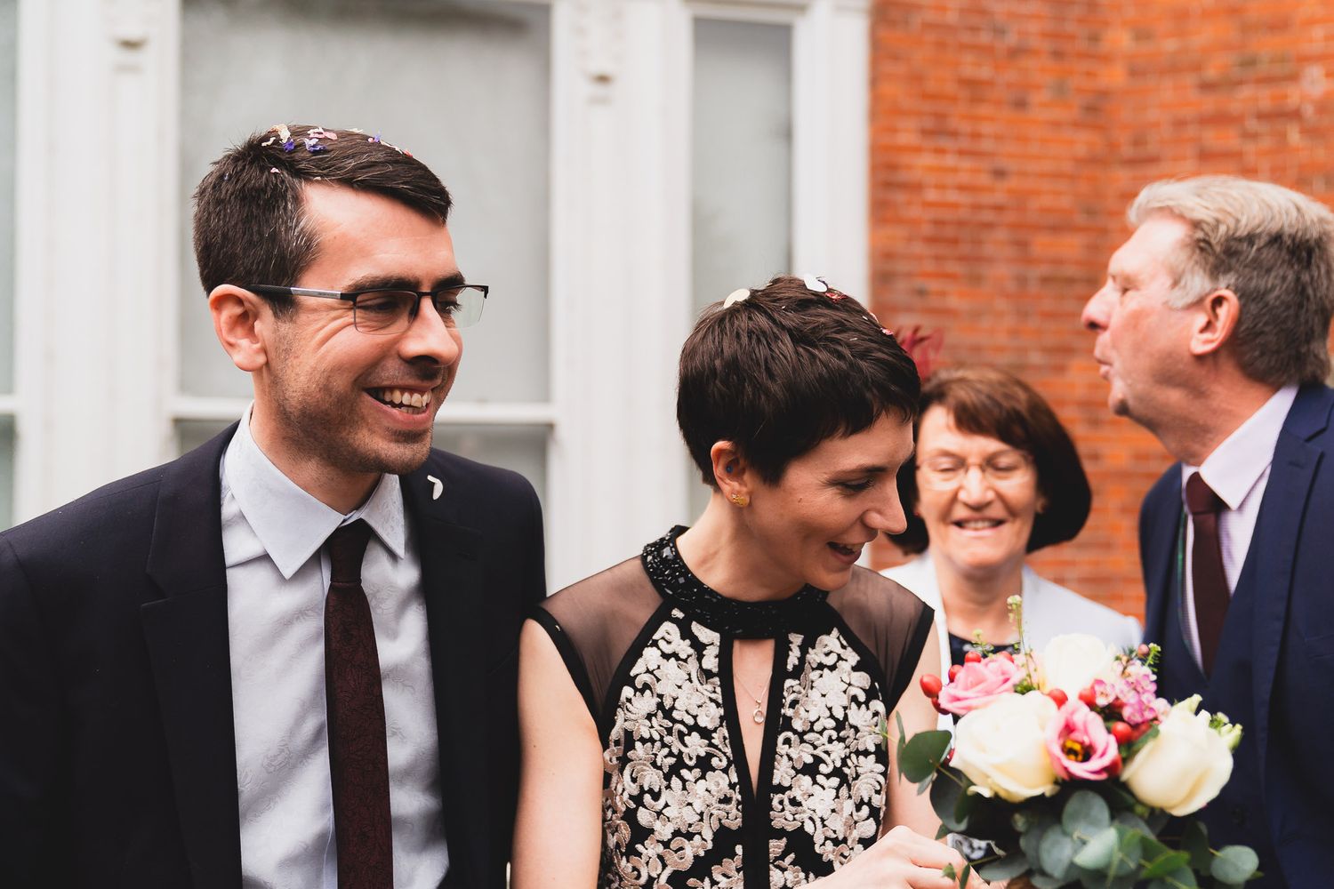 Happy bride and groom, as father blows confetti of his wife's hair.
