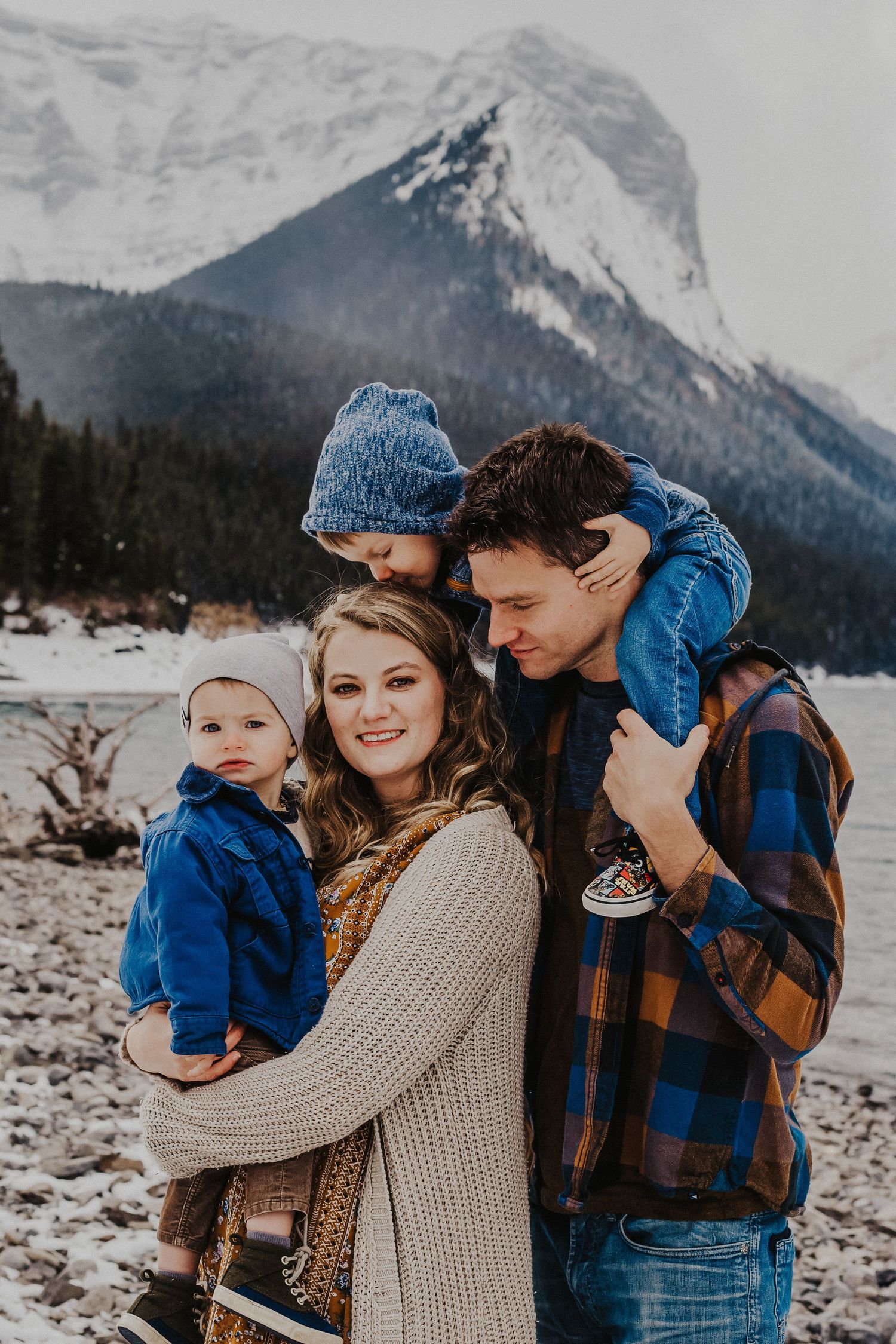 Mother holds baby boy while dad holds other boy who kisses mom