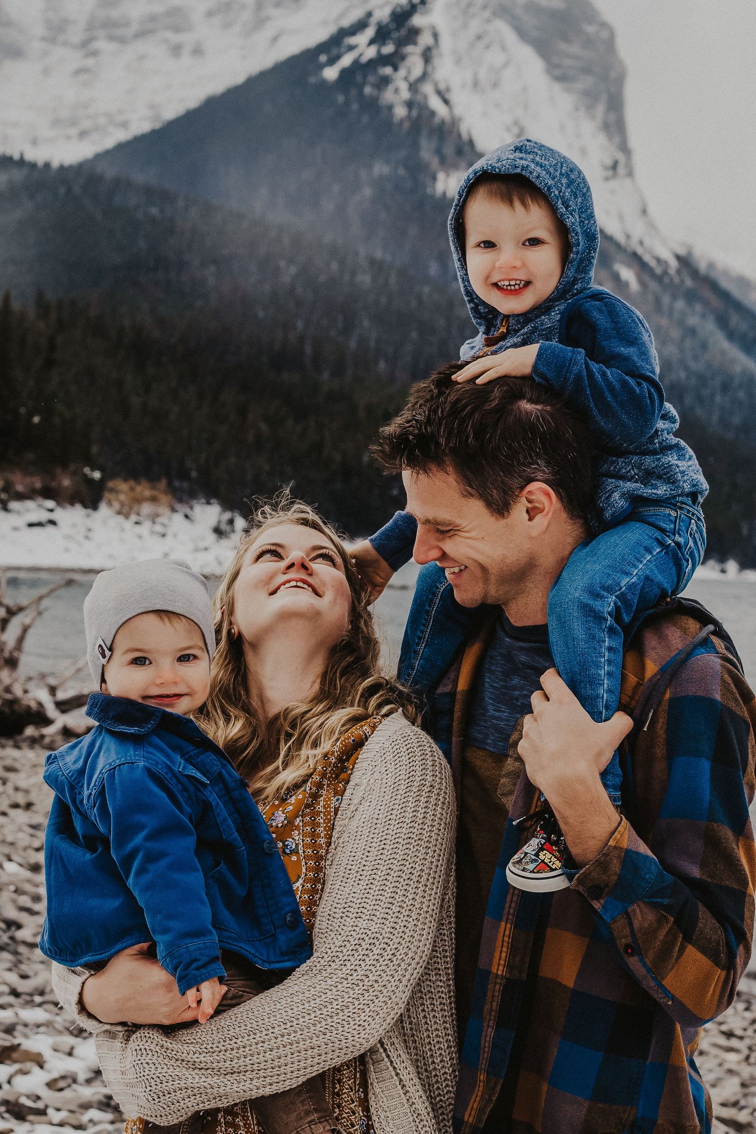 boy on dad's shoulders touches moms hair while she smiles at him