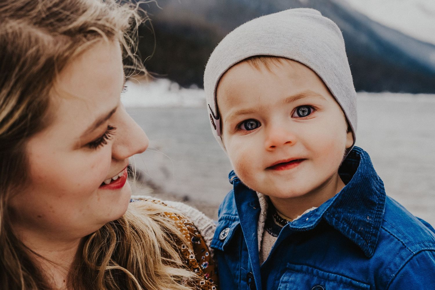 boy with beautiful eyes smiles at camera while mother holds him