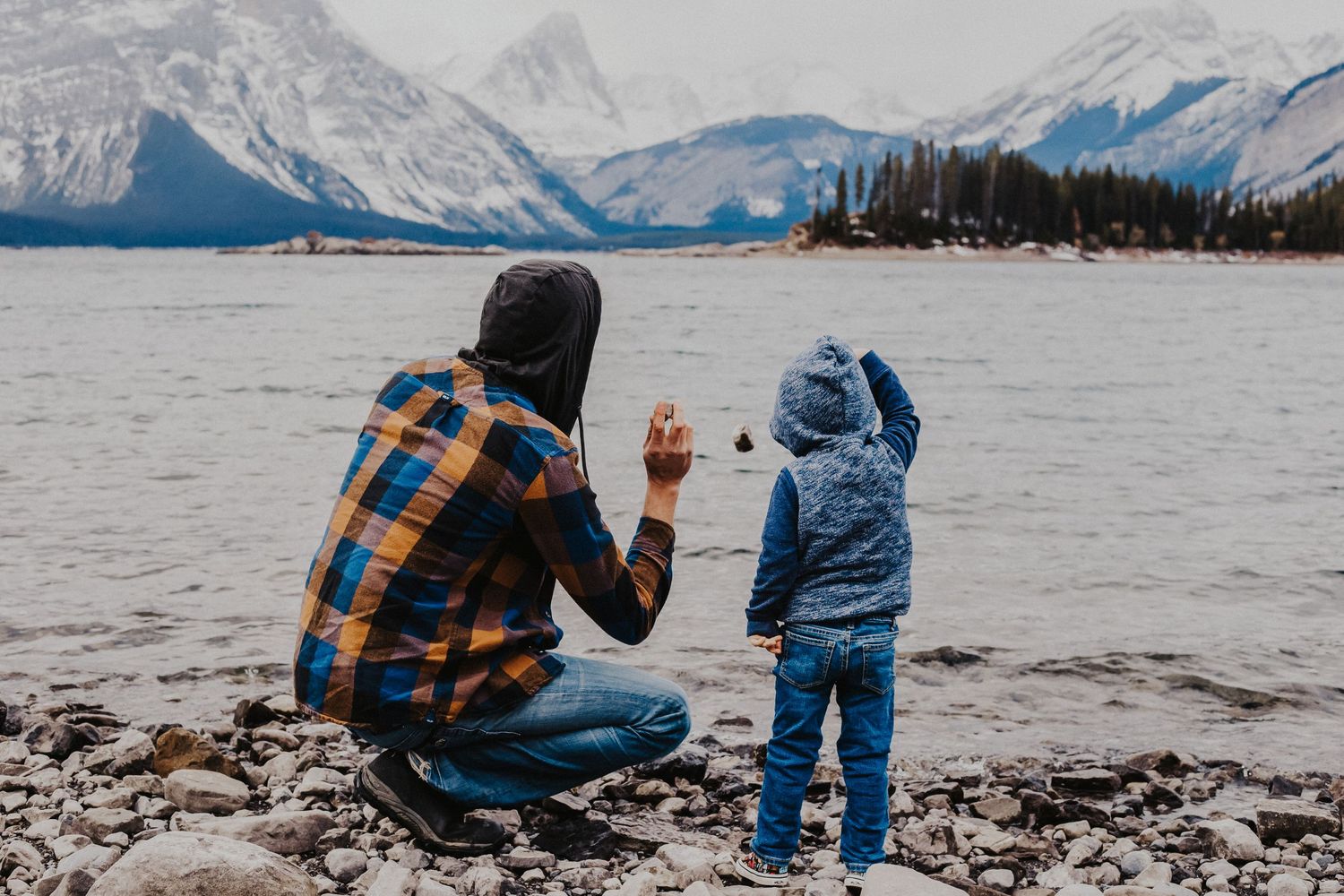 father and son throw rocks into mountain lake