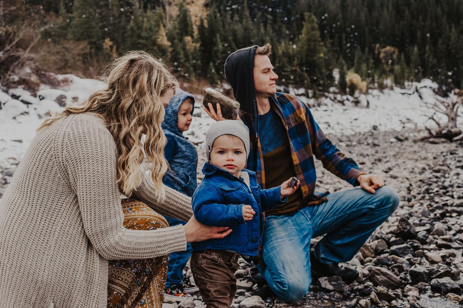 family of four crouch on lake shoreline to throw rocks