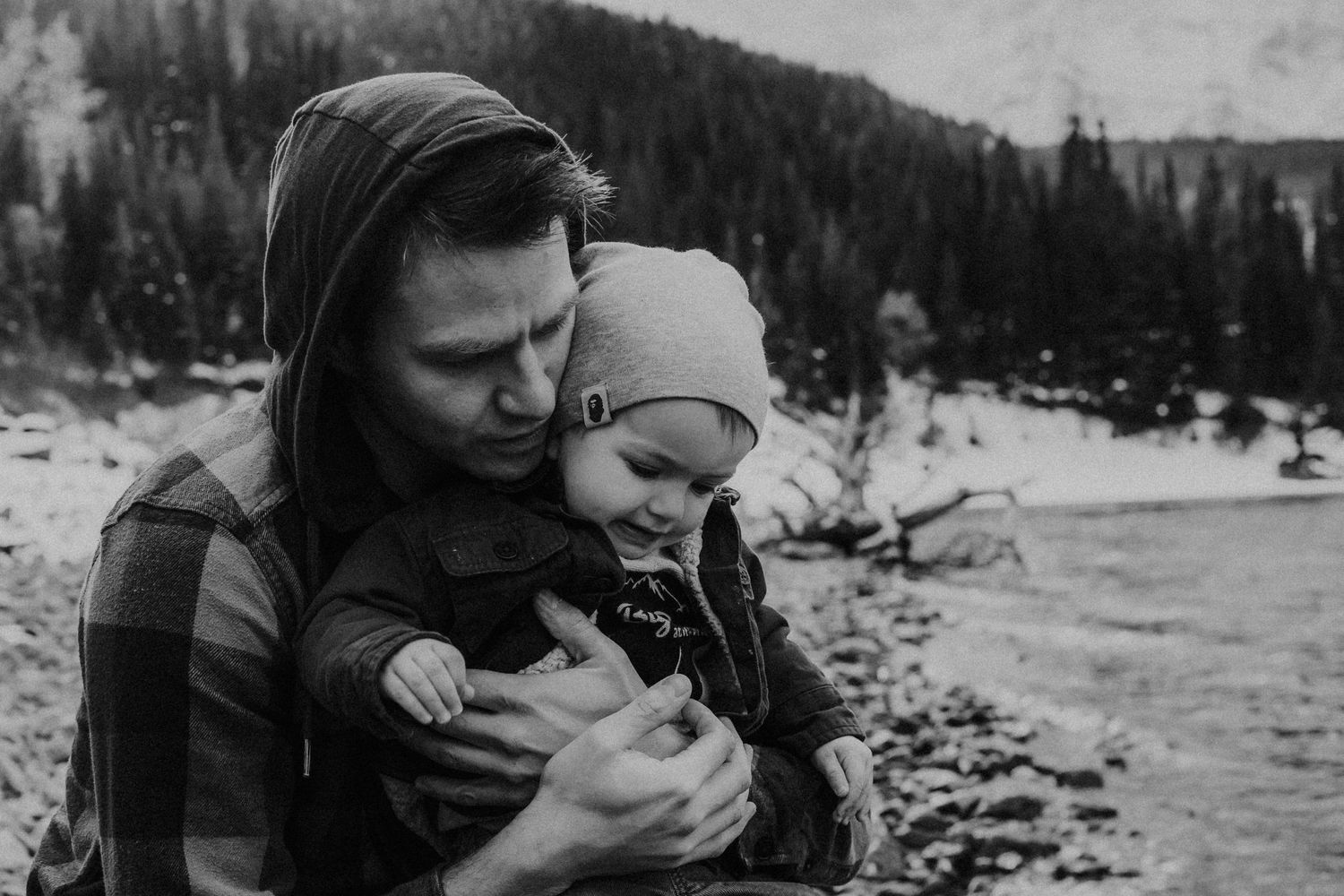 black and white photo of dad holding son on lake shoreline