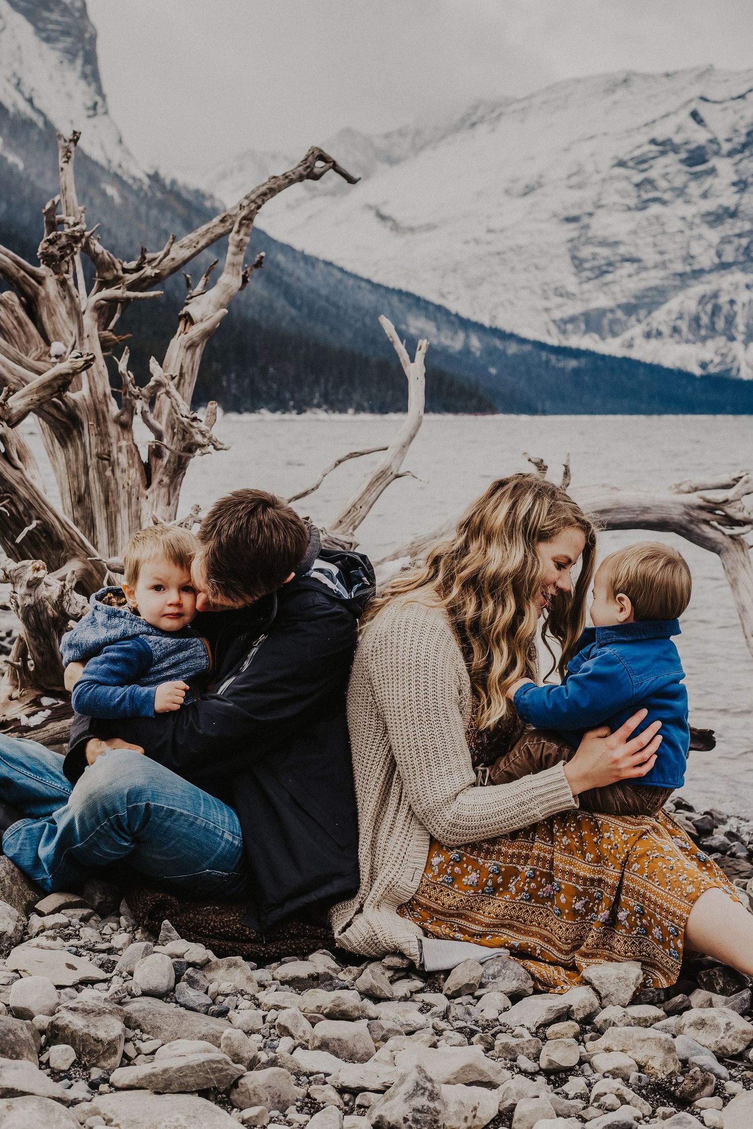 parents kiss and play with two sons on lake shoreline