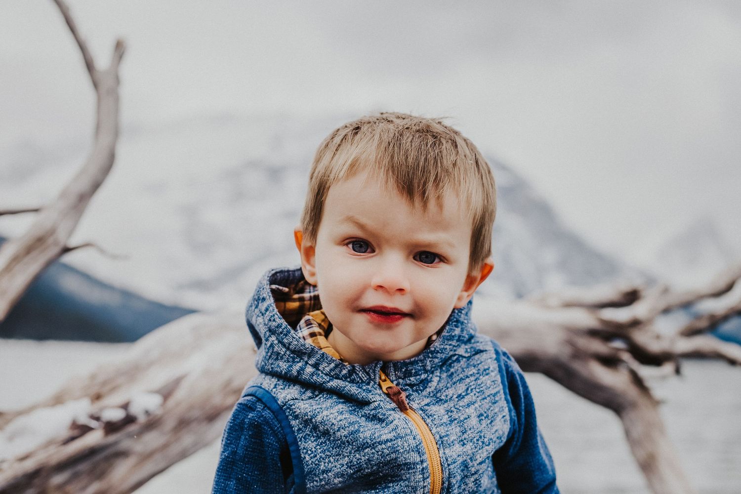 young boy in front of upper kananaskis lake smiles with one eyebrow arched