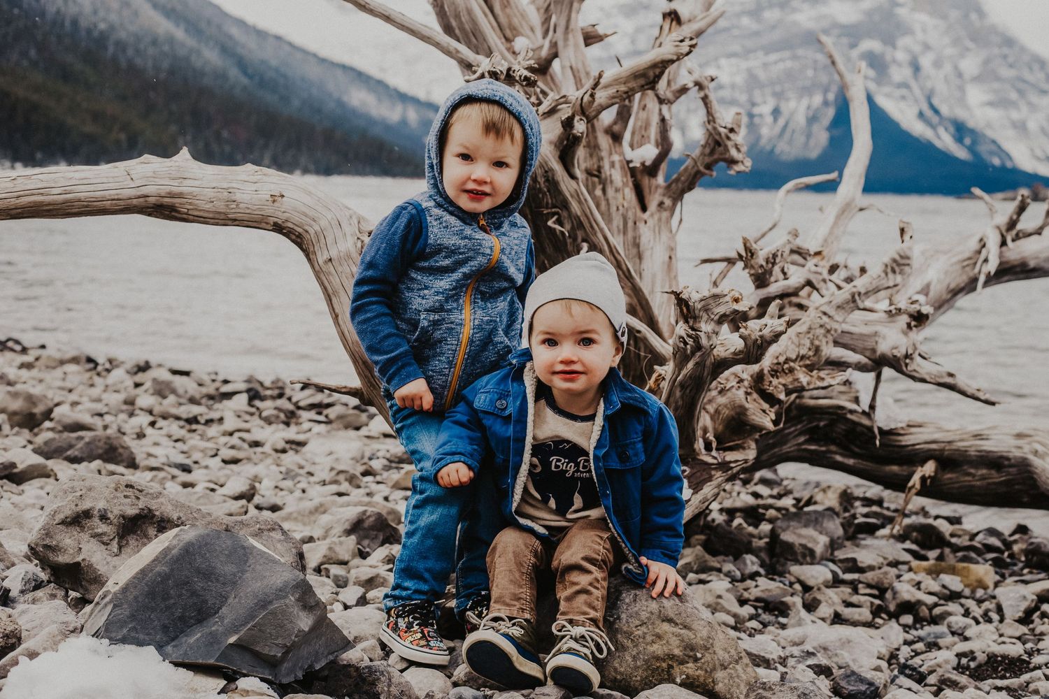 two boys in front of driftwood at mountain lake