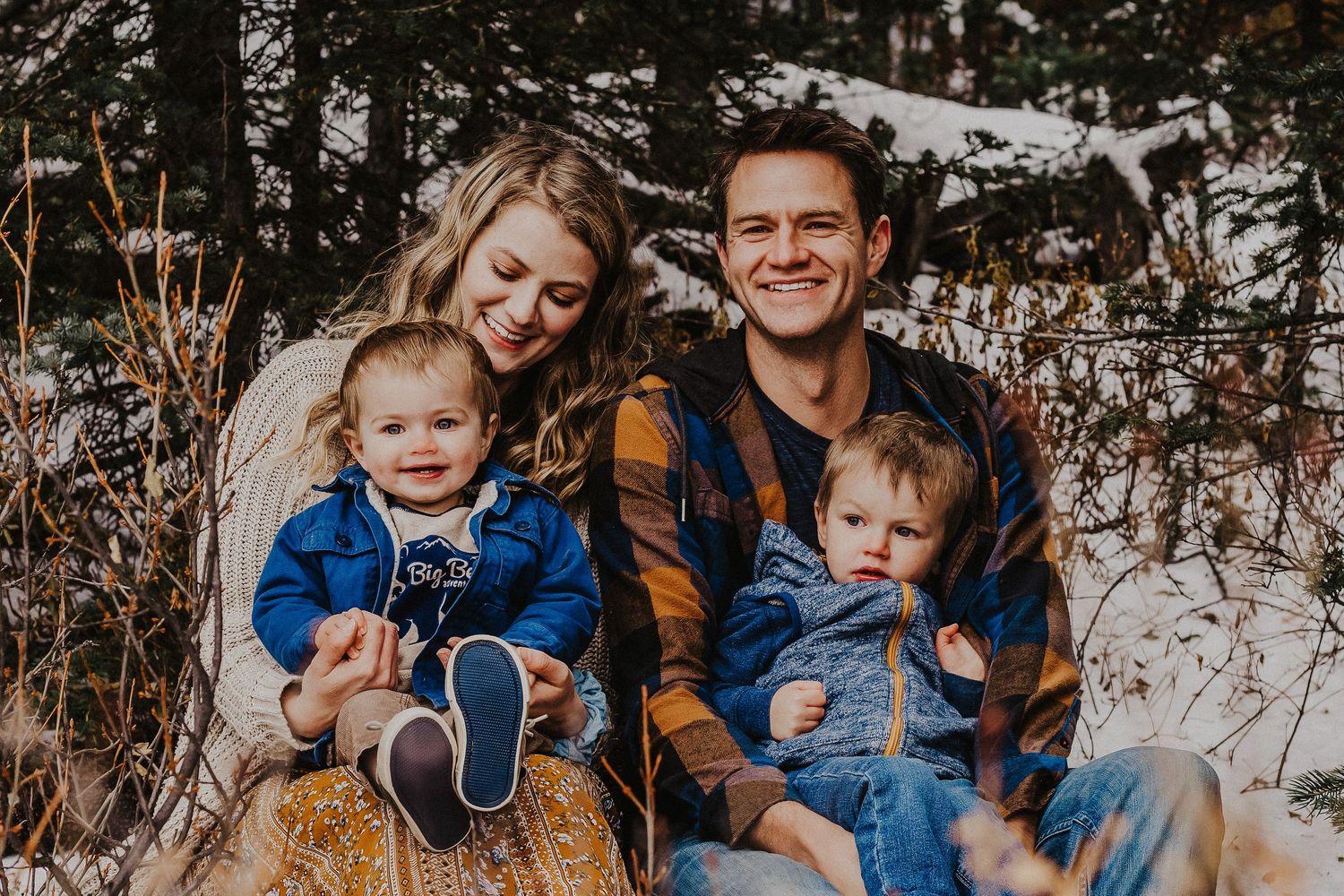 family sits in snowy trees and laughs