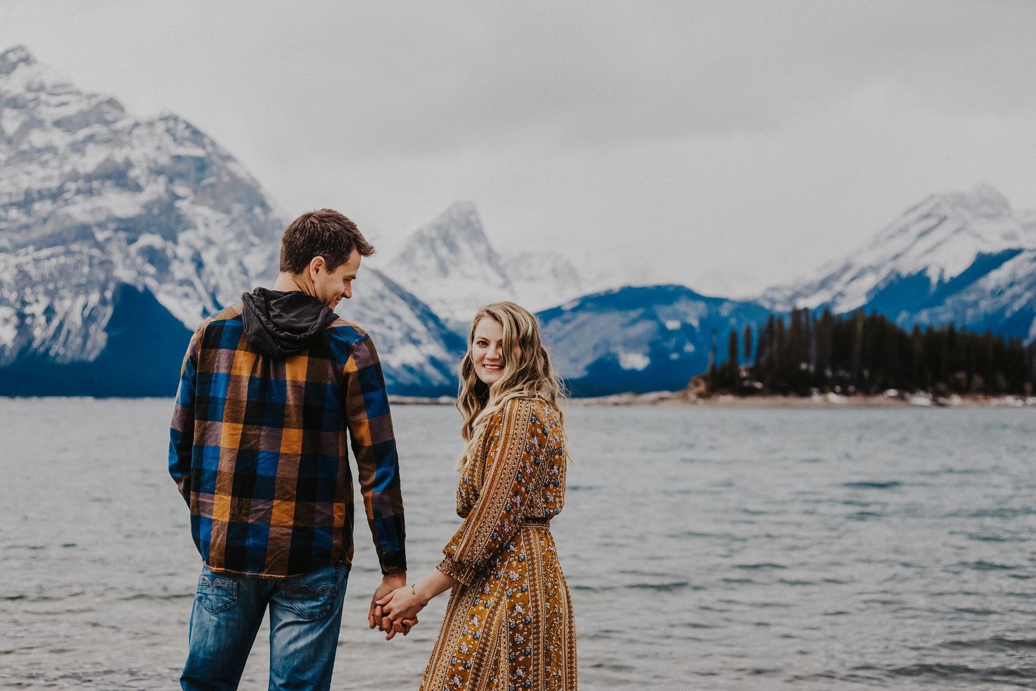 husband looks at wife who smiles while standing in front of kananaskis mountains