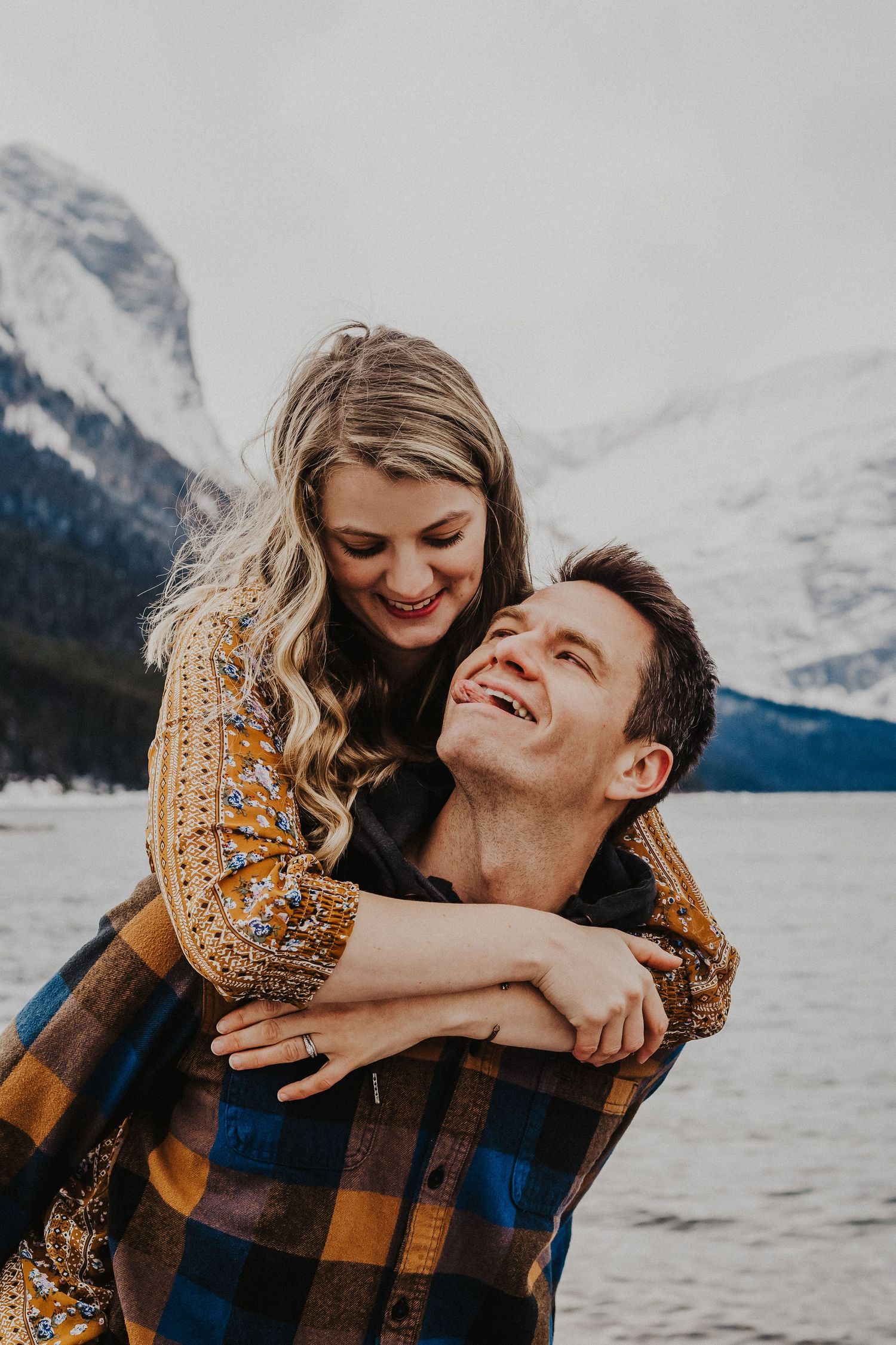 man sticks tongue out while smiling up at wife who is on his back
