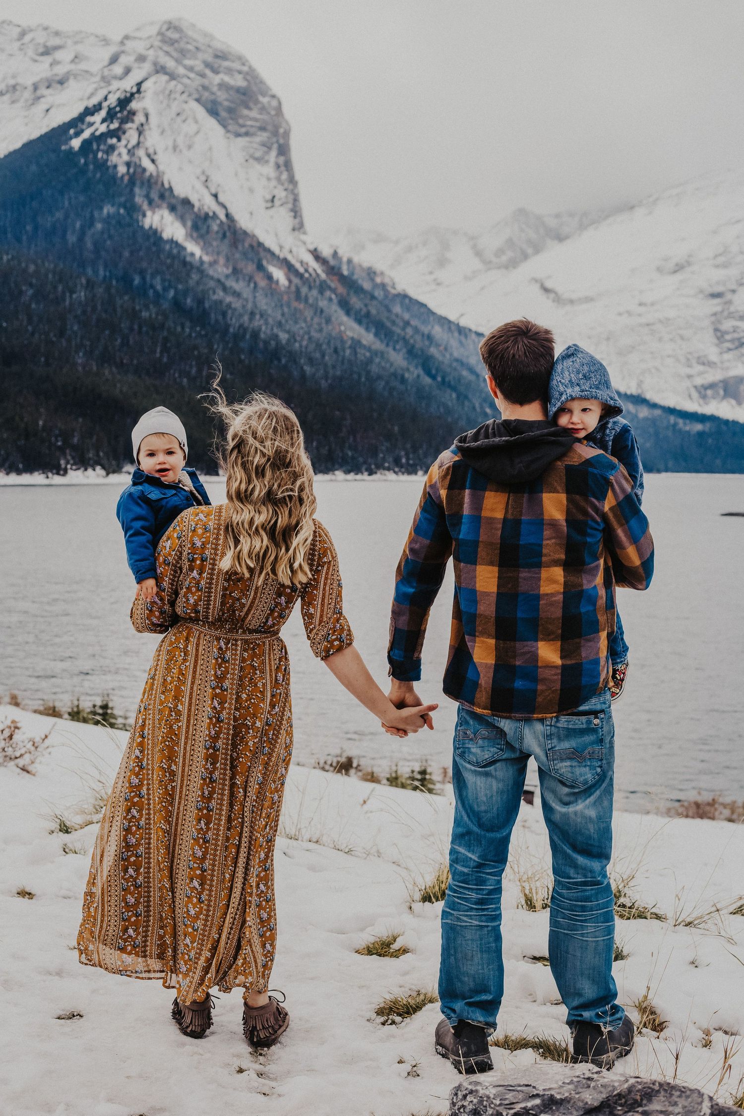 family stands and faces mountains while holding hands