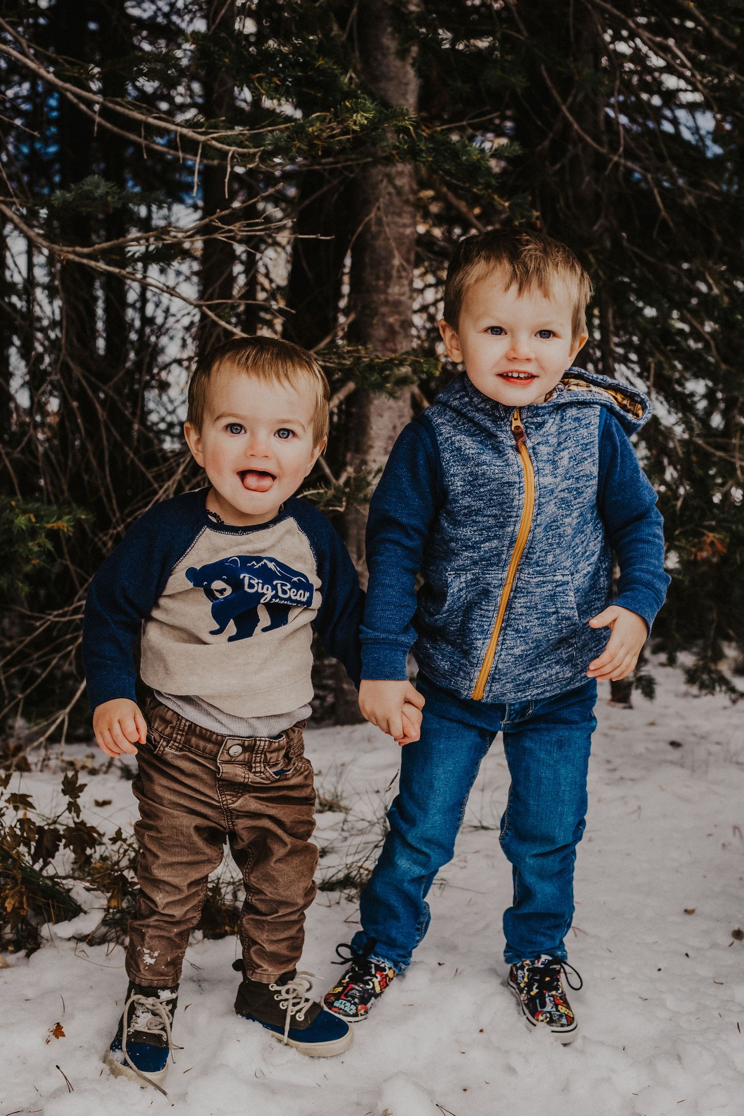 2 young boys hold hands in front of trees