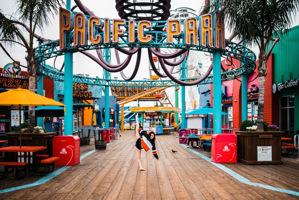 Girl dancing/doing the splits beneath the Pacific Pier sign at Santa Monica Pier. Colorful image.