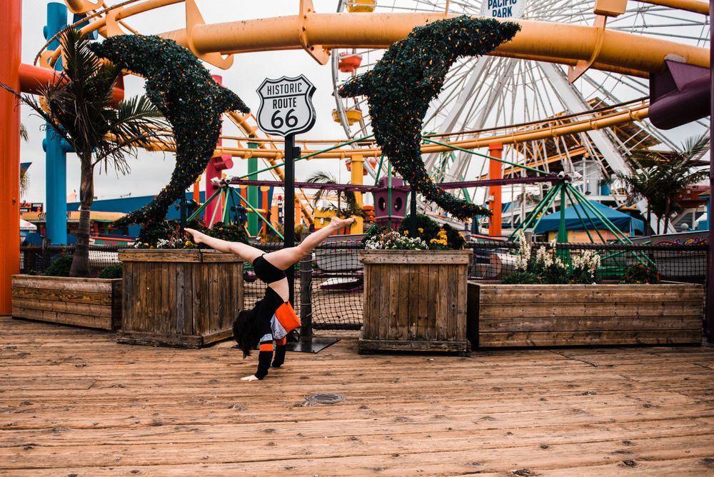 Girl doing a cartwheel while dancing in front of the rollercoaster at Santa Monica Pier