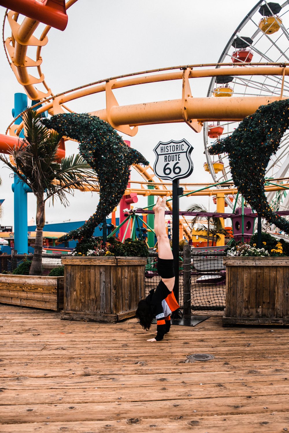 Girl doing a handstand while dancing in front of a rollercoaster during a Santa Monica Pier photoshoot