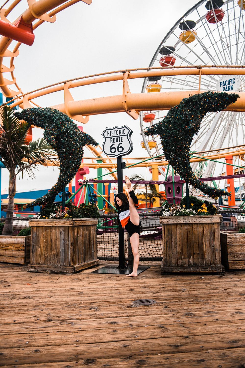 Girl doing the splits while dancing in front of a rollercoaster during a Santa Monica Pier photoshoot