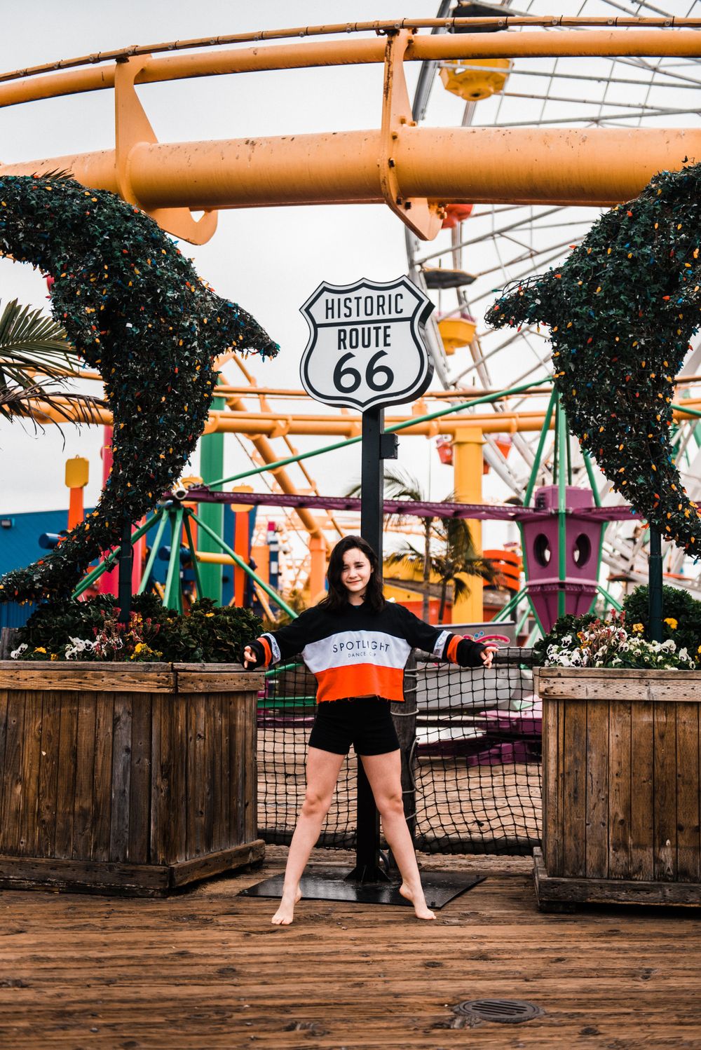 Girl standing on her toes while dancing in front of a rollercoaster during a Santa Monica Pier photoshoot