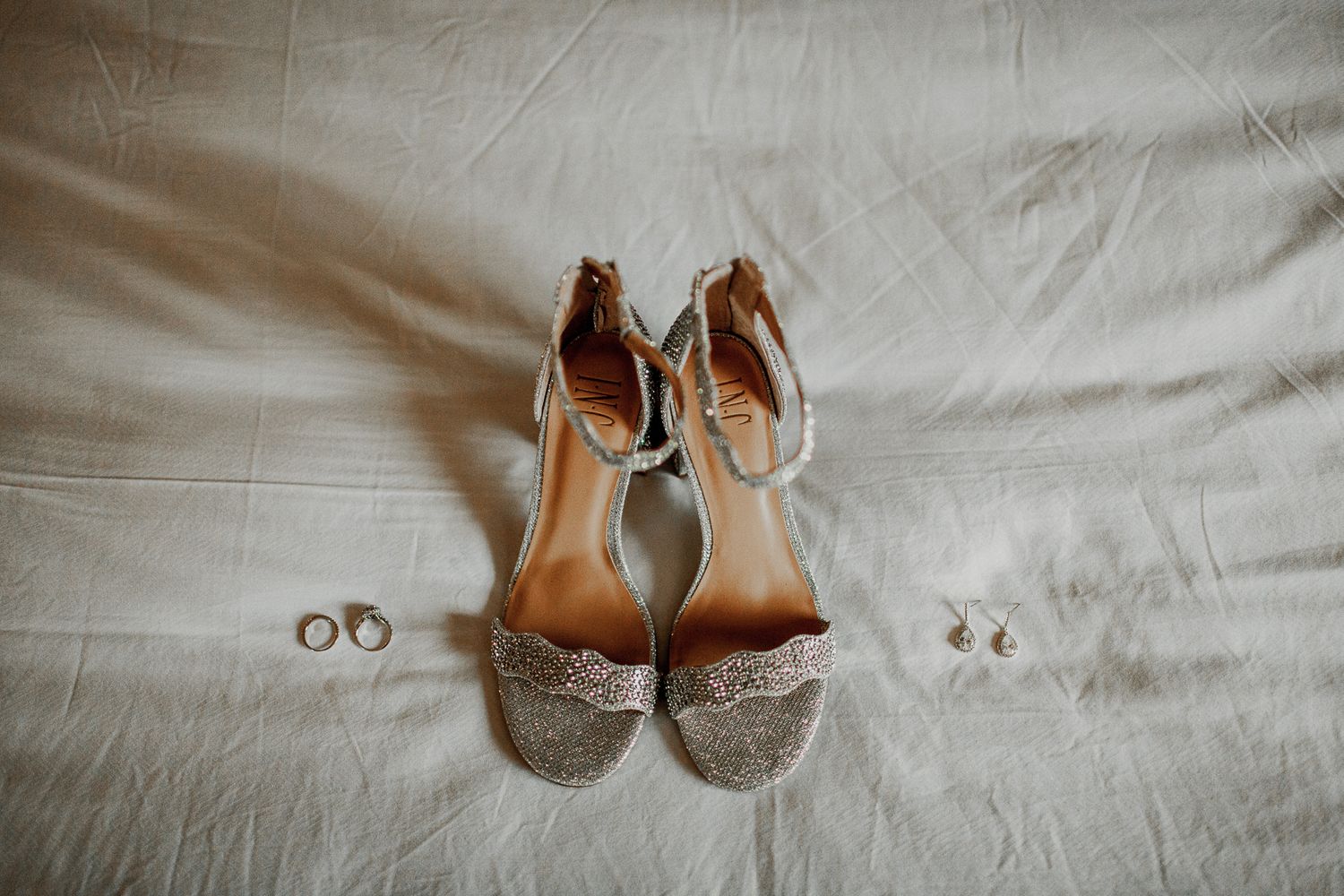 bride shoes, earrings, and rings on top of bed