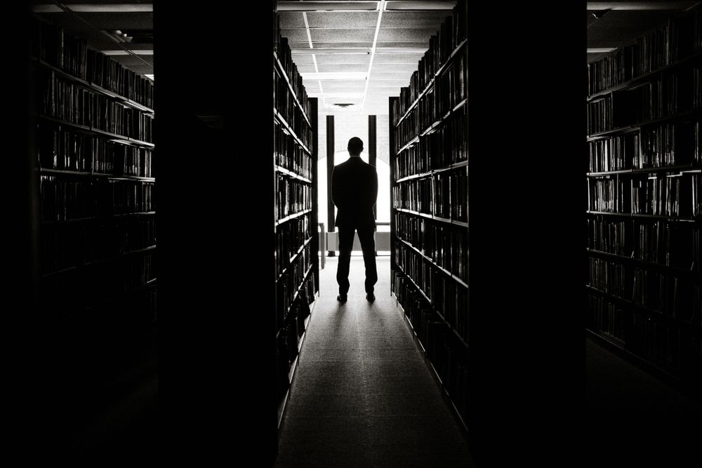 groom-walking-down-book-aisle-for-first-look-wedding-cowles-library-desmoines-iowa-raelyn-ramey-photography