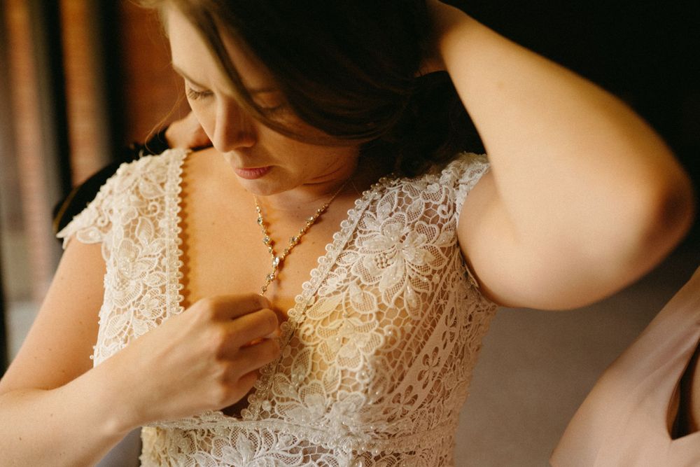 bride-getting-necklace-on-getting-ready-wedding-cowles-library-desmoines-iowa-raelyn-ramey-photography
