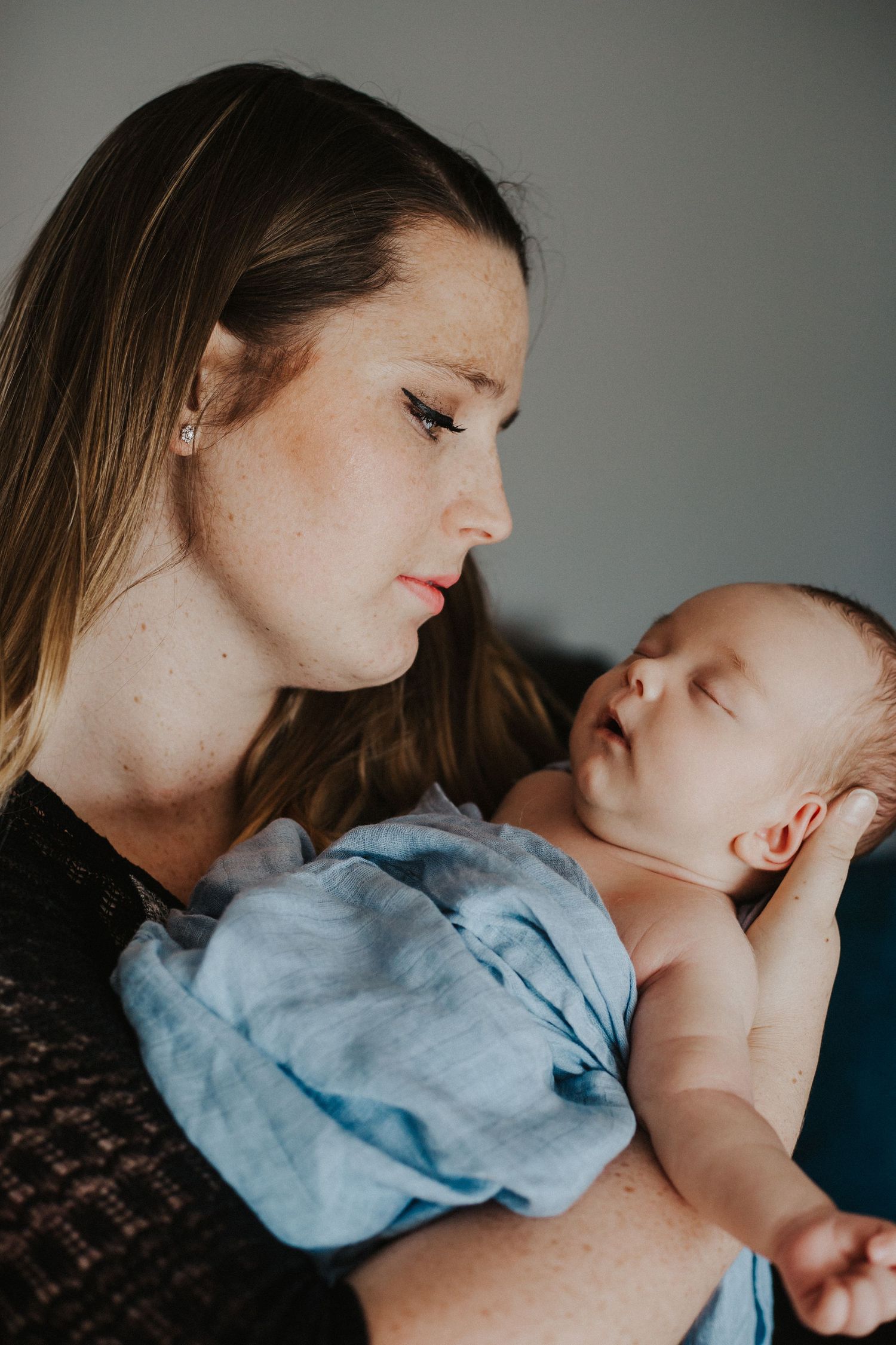 mom looks lovingly at newborn baby boy as he sleeps in her arms